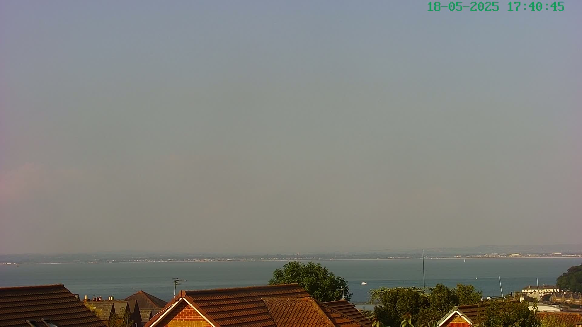 A hazy, calm day overlooks a wide expanse of water, with rooftops and vegetation in the foreground.