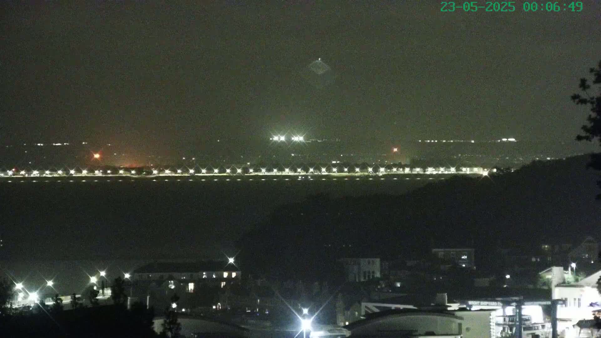 A nighttime view of a city across a body of water, under a hazy sky.