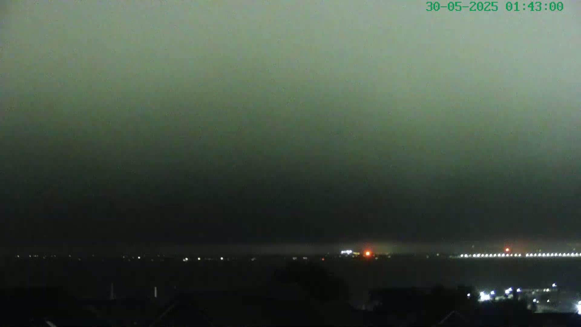 A nighttime, hazy view shows a distant, dimly lit cityscape across a body of water.