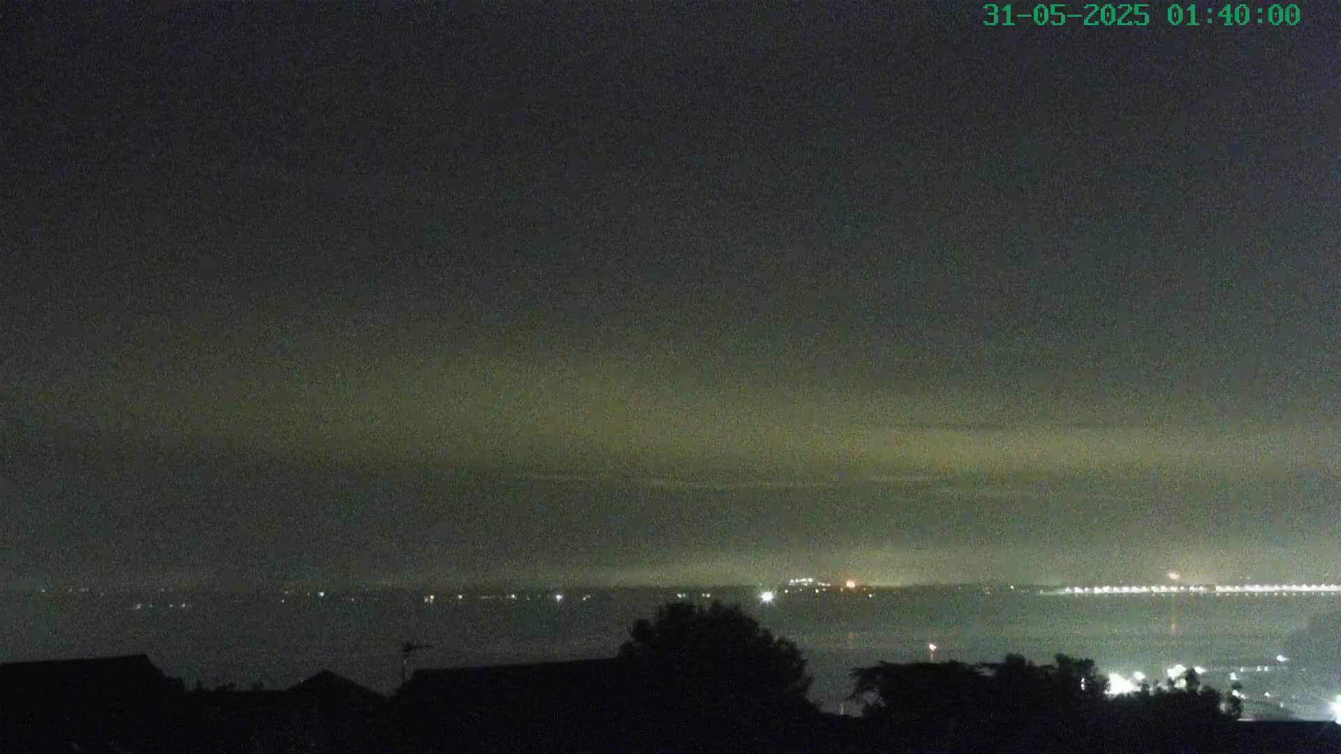 A nighttime view of a body of water with distant lights on the opposite shore under a hazy, dark sky.