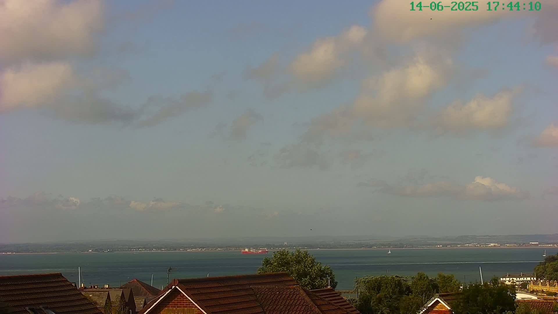 A partly cloudy day overlooks a calm body of water with a distant shoreline and rooftops in the foreground.