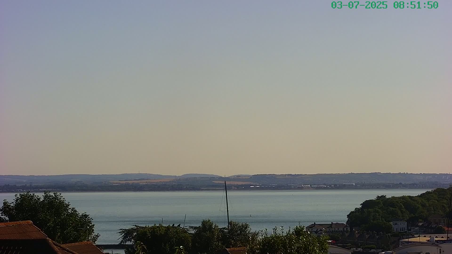 A calm body of water stretches to a distant shoreline under a hazy, light-colored sky.