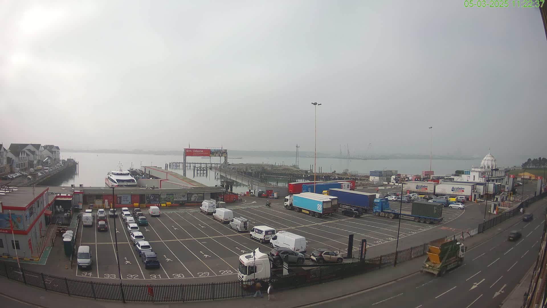 A ferry terminal with a mostly empty parking lot and several trucks, viewed on a foggy day.
