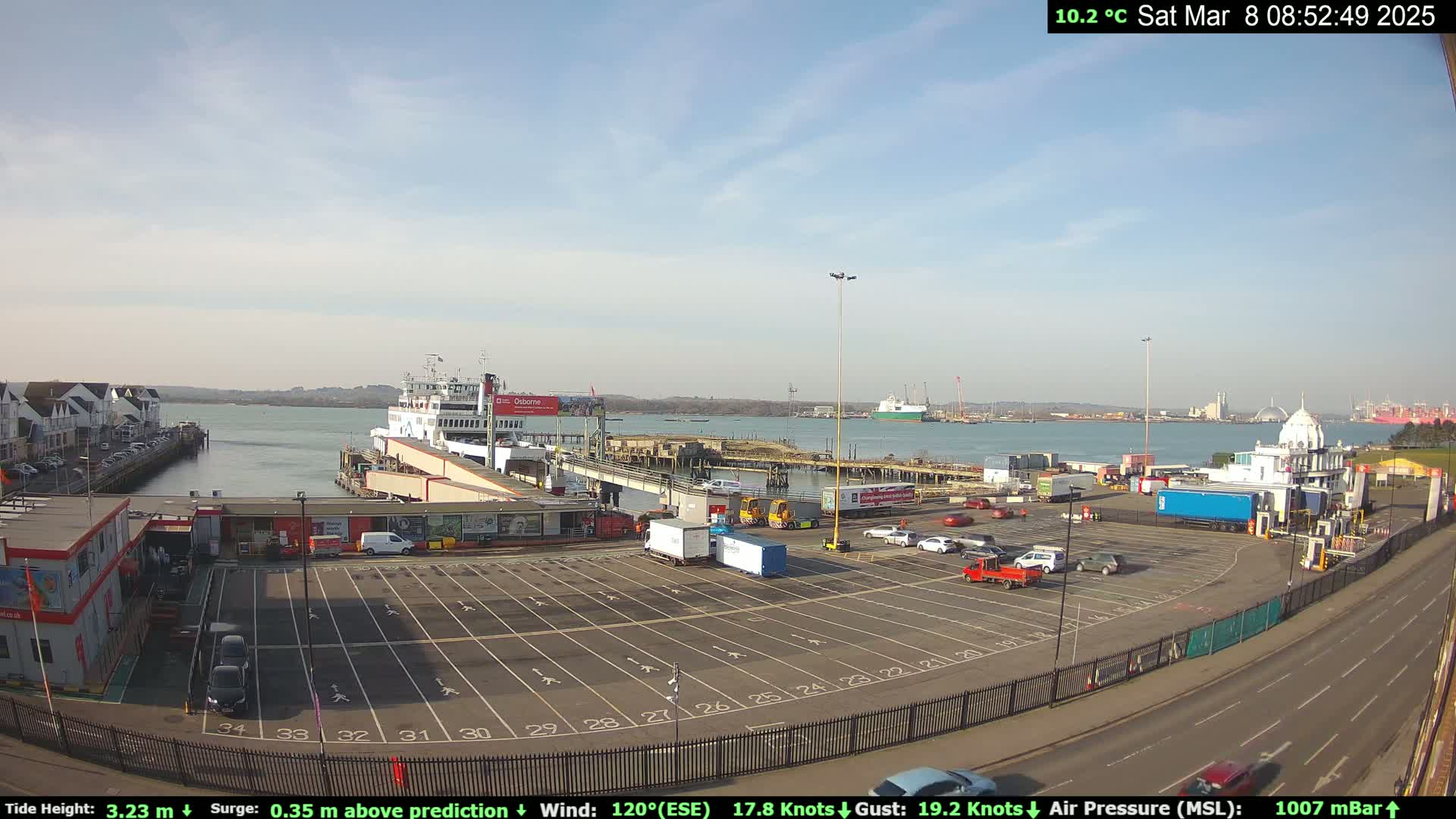 A ferry is docked at a terminal on a sunny day with a calm body of water visible in the background.