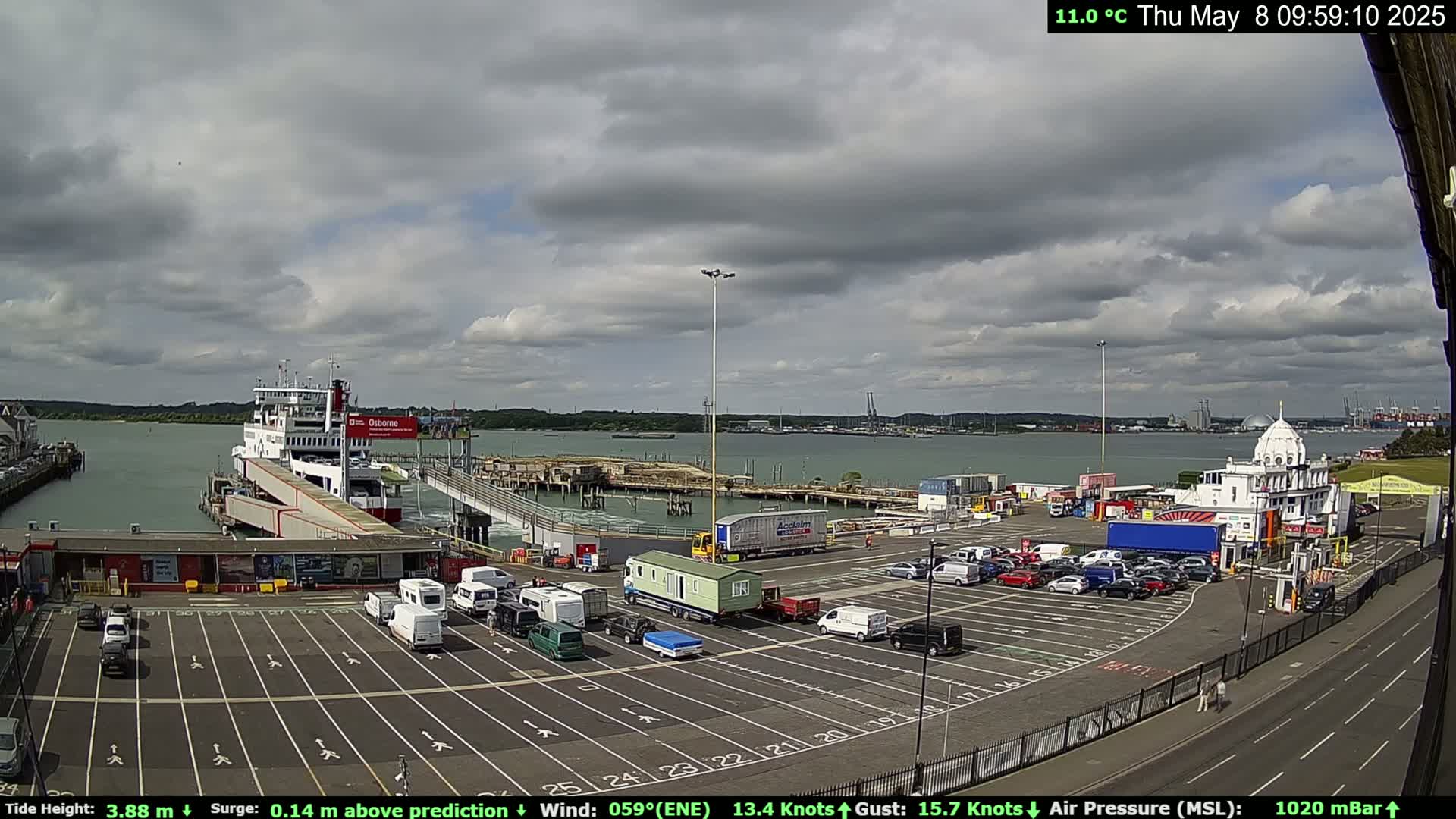 A ferry is docked at a terminal with a partly cloudy sky and a moderate wind.