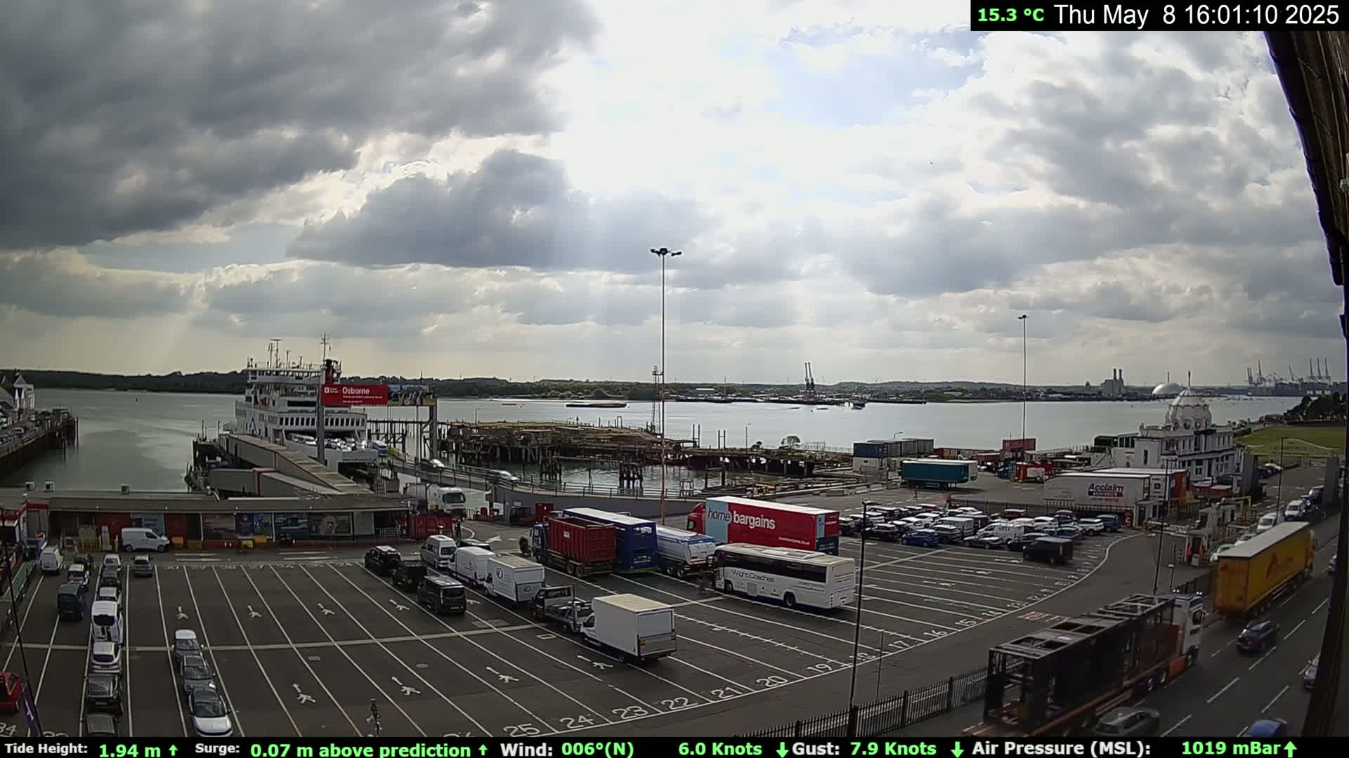 A ferry is docked at a terminal with a partly cloudy sky and a calm body of water in the background.
