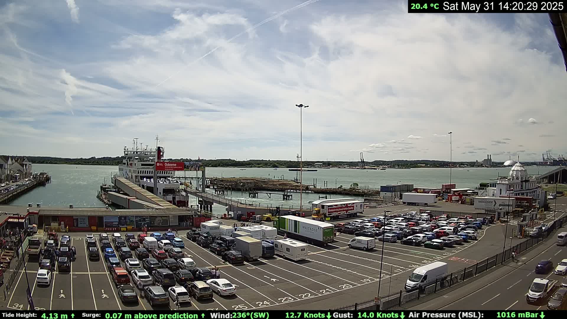 A ferry is docked at a terminal, surrounded by a large parking lot full of cars and other vehicles, under a partly cloudy sky.