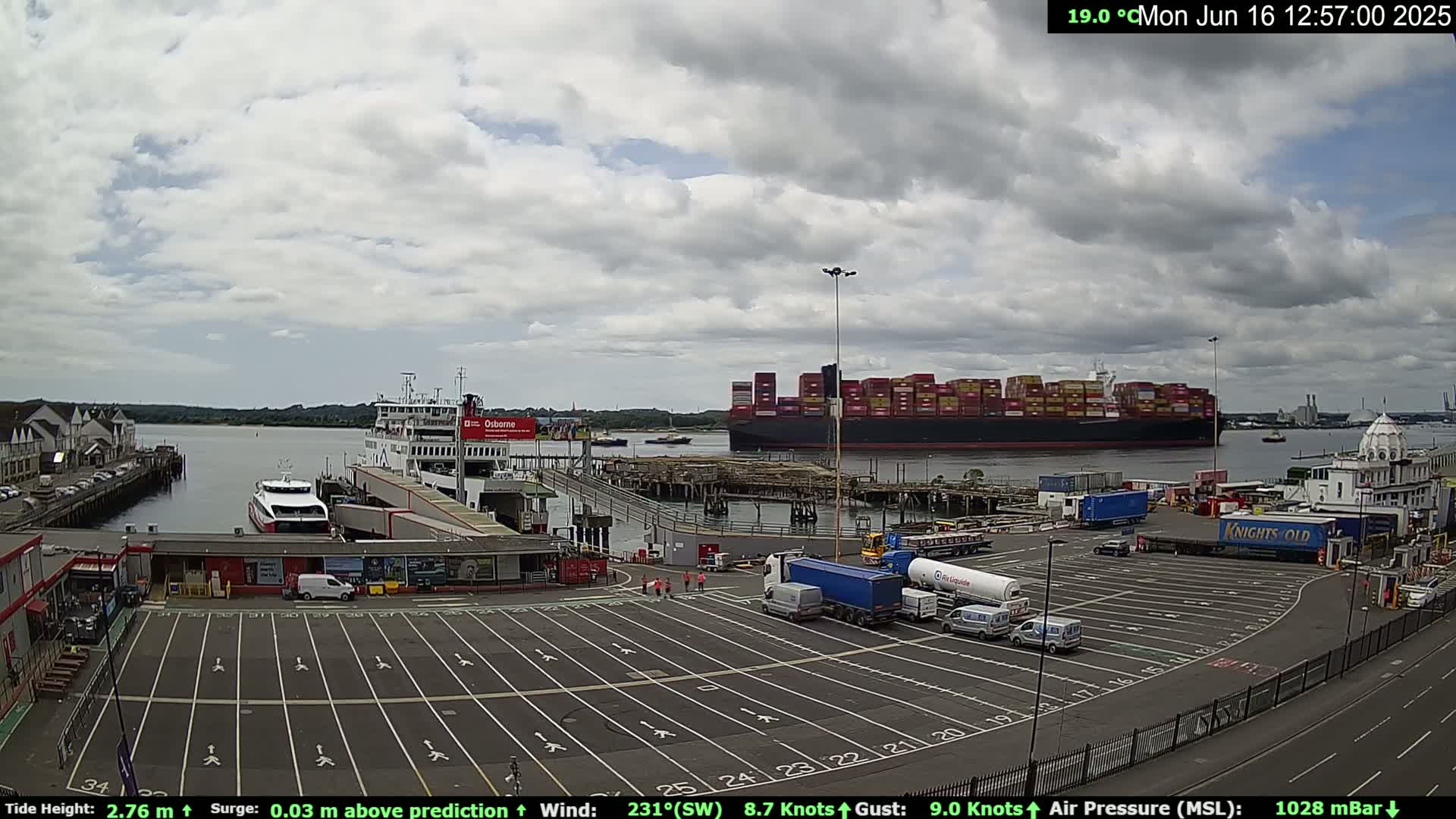 A ferry terminal with a large container ship in the harbor on a partly cloudy day.