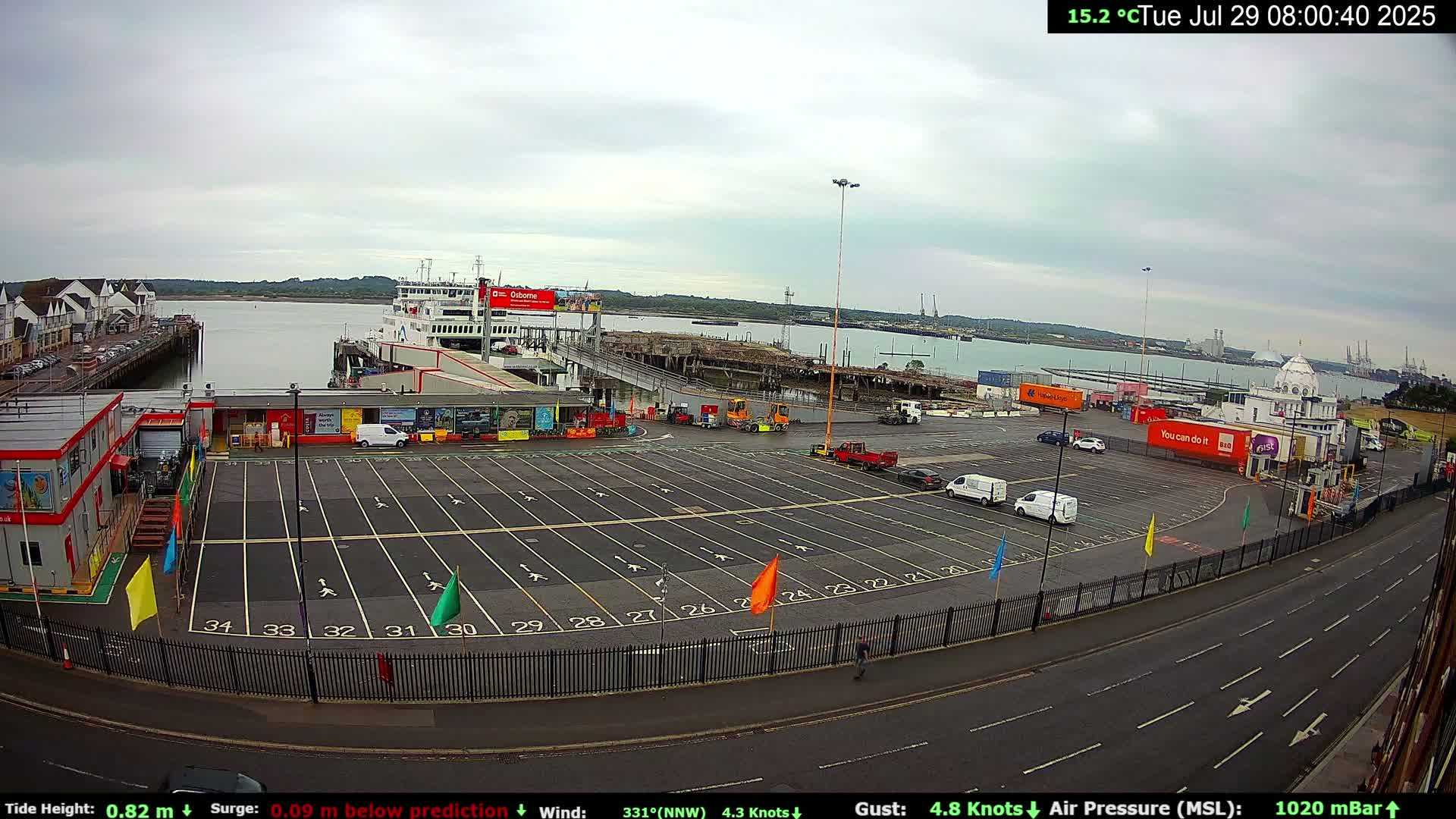 A ferry is docked at a terminal with a mostly empty parking lot and overcast skies.