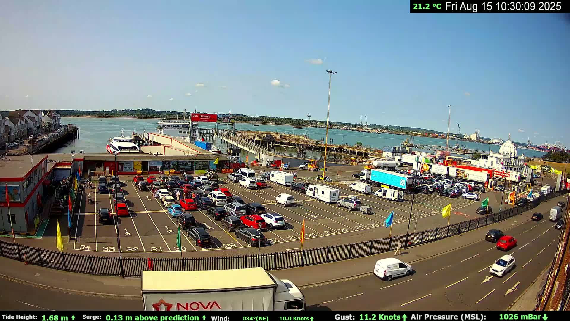 A ferry is docked at a terminal with a mostly empty parking lot and overcast skies.