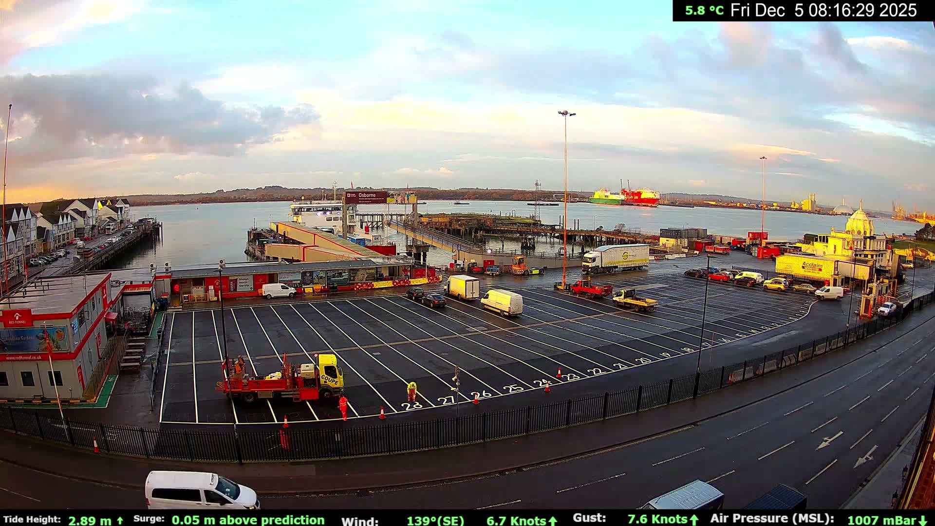 A cool and wet 5.8 °C early morning at a busy ferry terminal and port, where various vehicles, terminal buildings, and people are visible alongside multiple large ships on the water under a partly cloudy sky with soft, warm light.