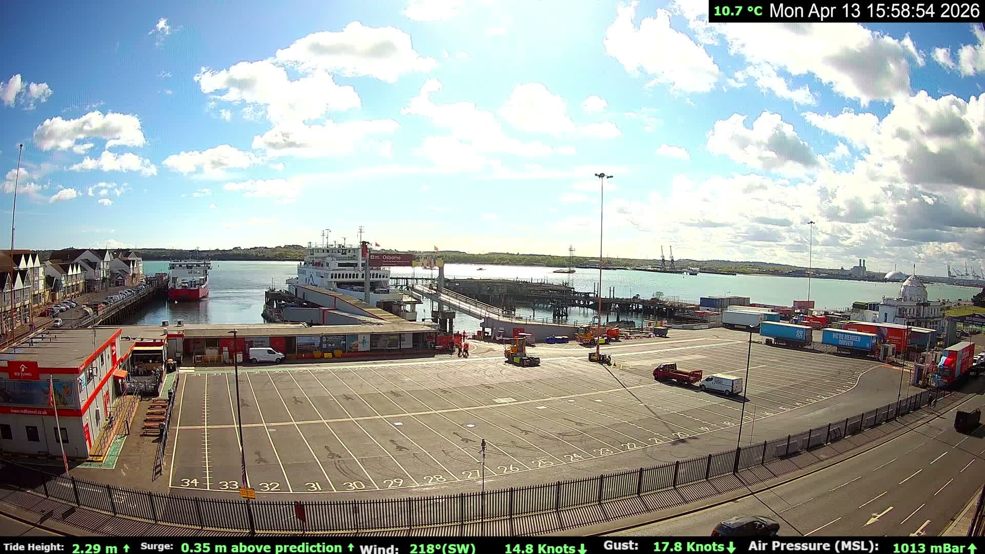 A cool and wet 5.8 °C early morning at a busy ferry terminal and port, where various vehicles, terminal buildings, and people are visible alongside multiple large ships on the water under a partly cloudy sky with soft, warm light.