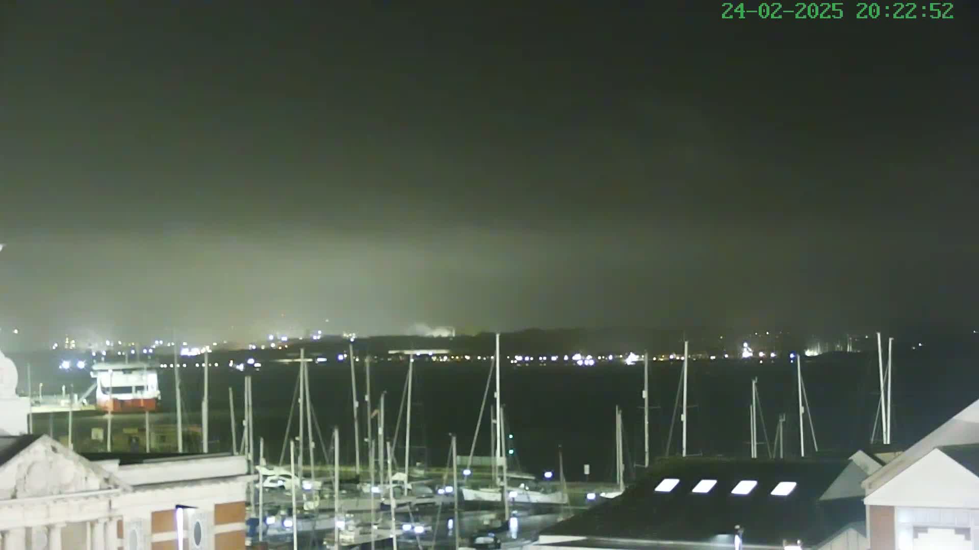 A nighttime view of a harbor filled with docked sailboats under a hazy, dark sky.