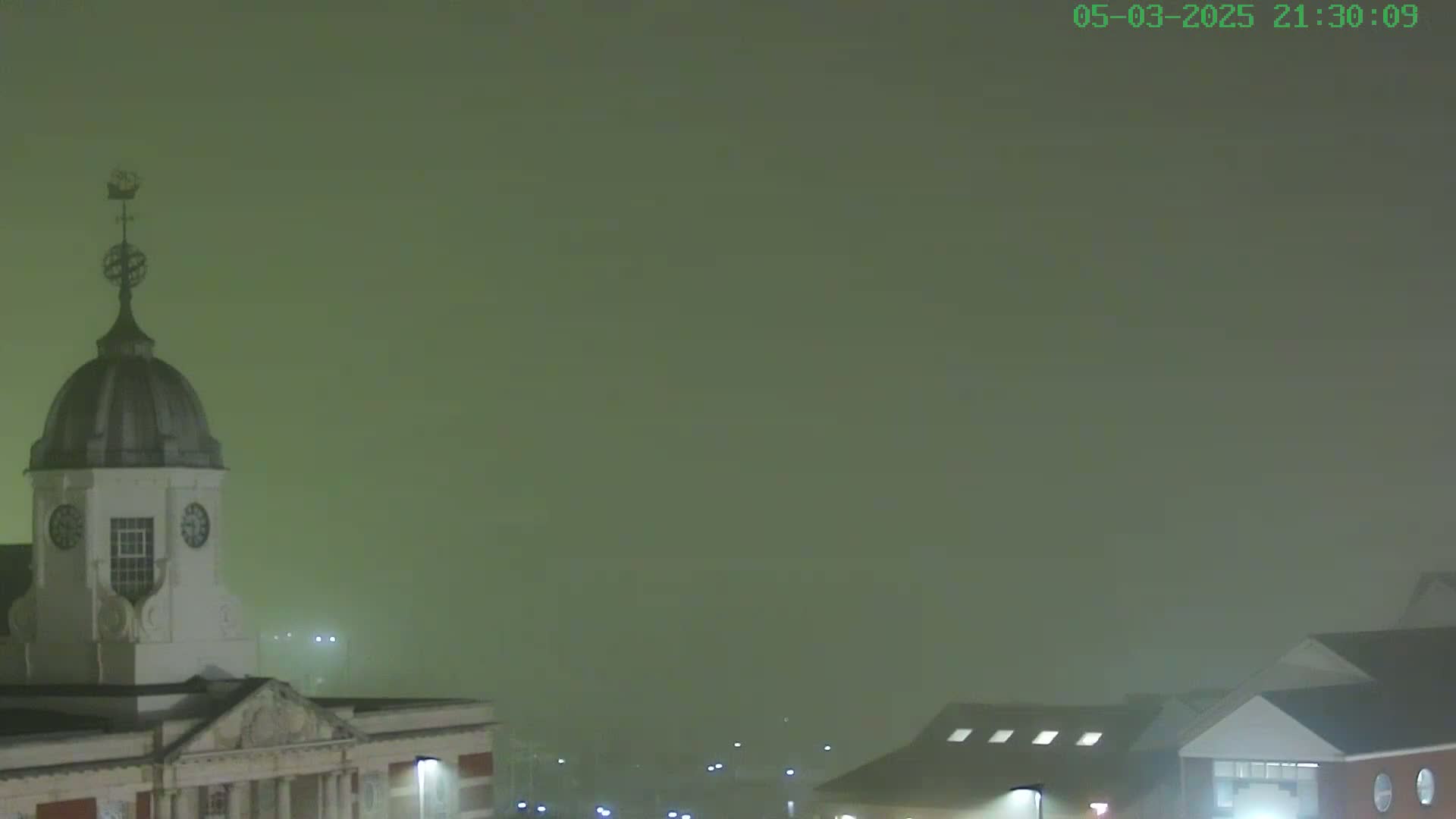 A nighttime view of a building with a domed clock tower shrouded in thick fog.