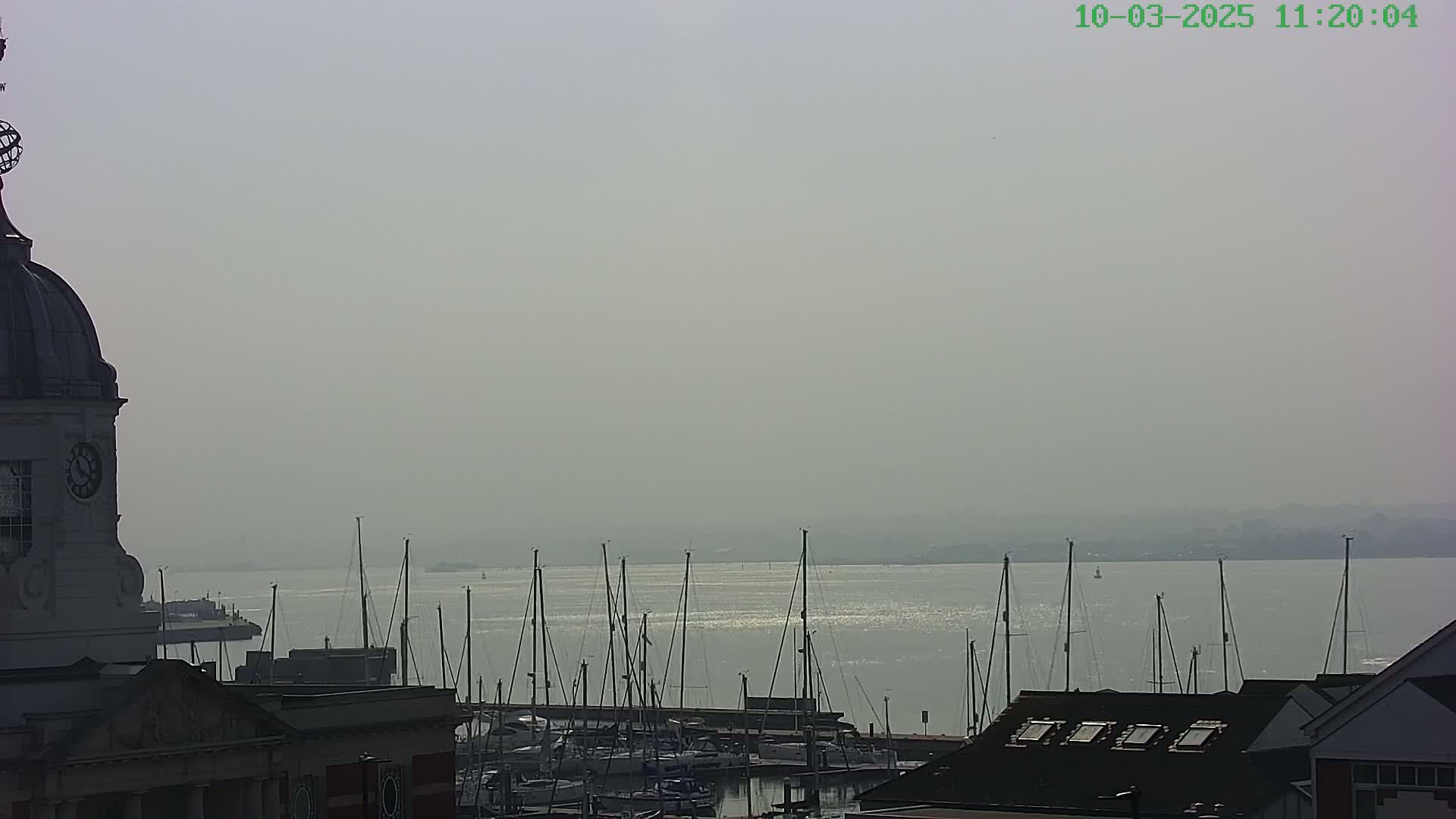 A hazy view of a harbor filled with sailboats, seen from atop a building with a dome and clock tower.