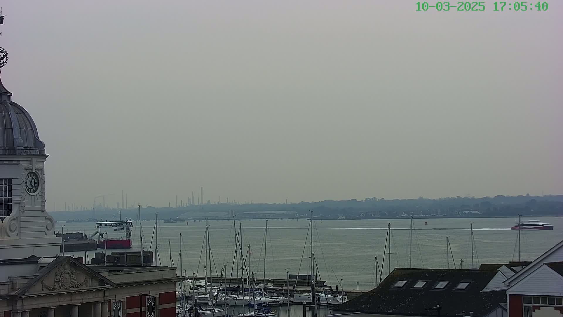A hazy view from a clock tower shows a harbor filled with sailboats and a ferry, with an industrial skyline visible in the distance.