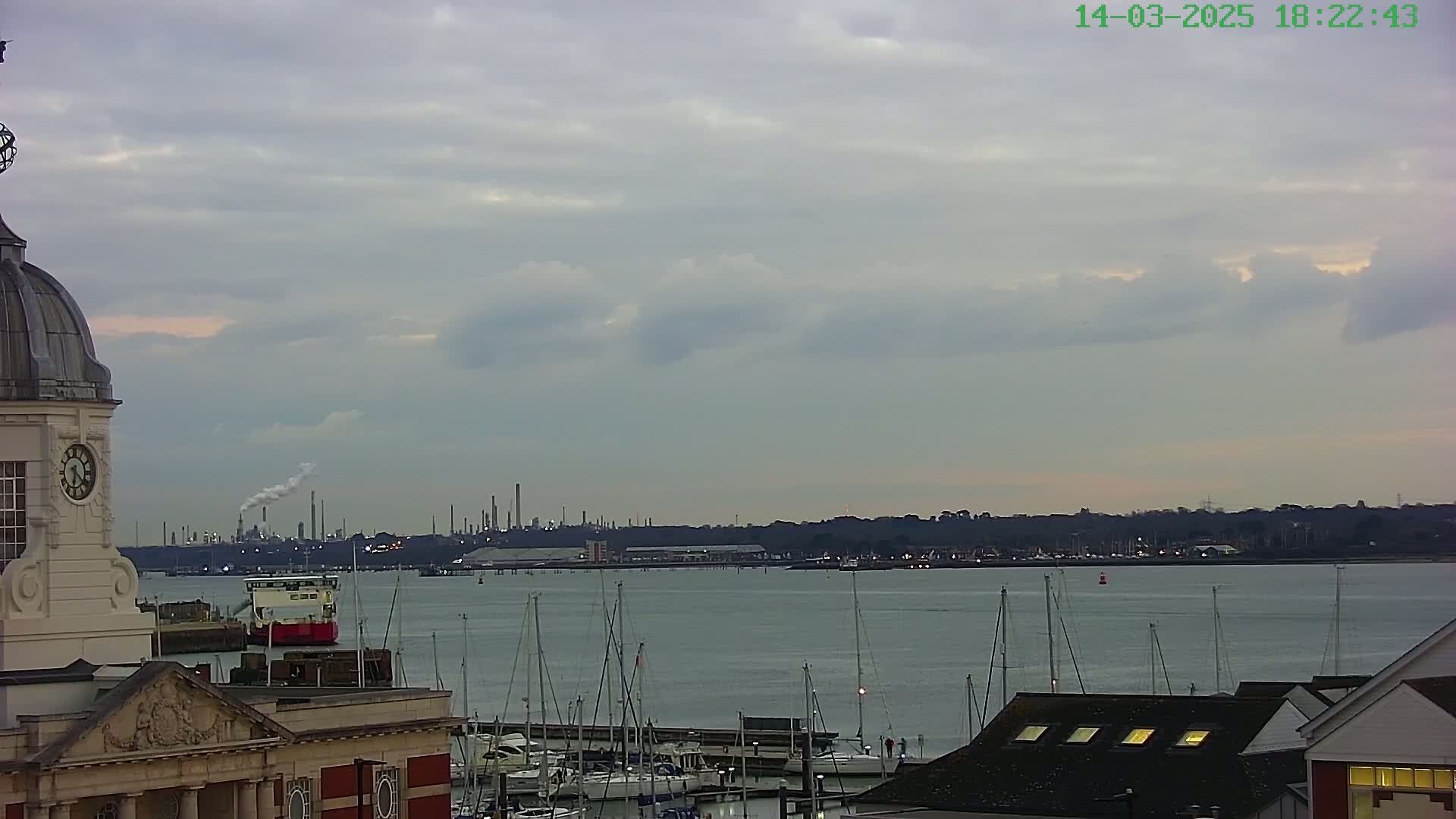 A view from atop a building shows a harbor filled with sailboats, an industrial plant in the distance, and an overcast sky.