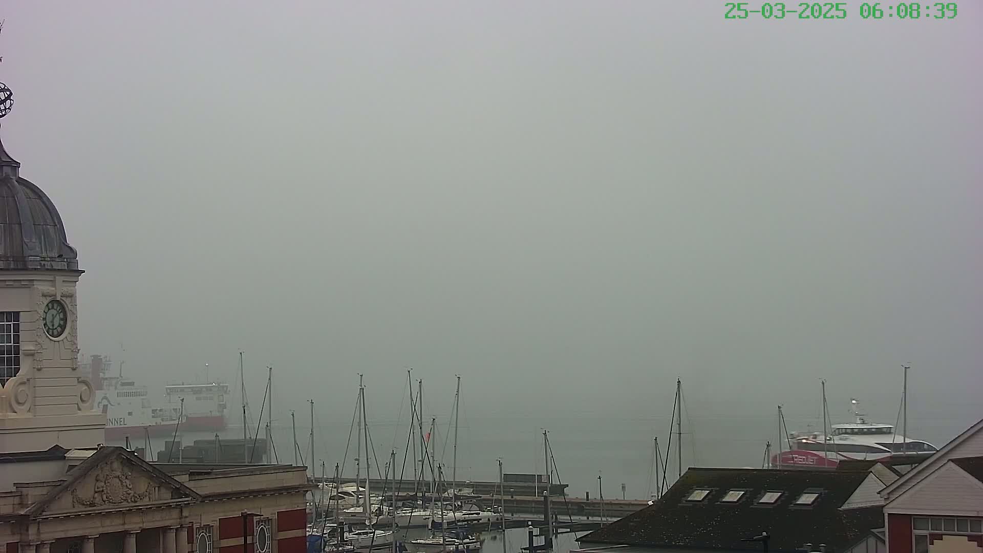 A foggy harbor scene shows a portion of a clock tower, docked boats, and a ferry in the distance.