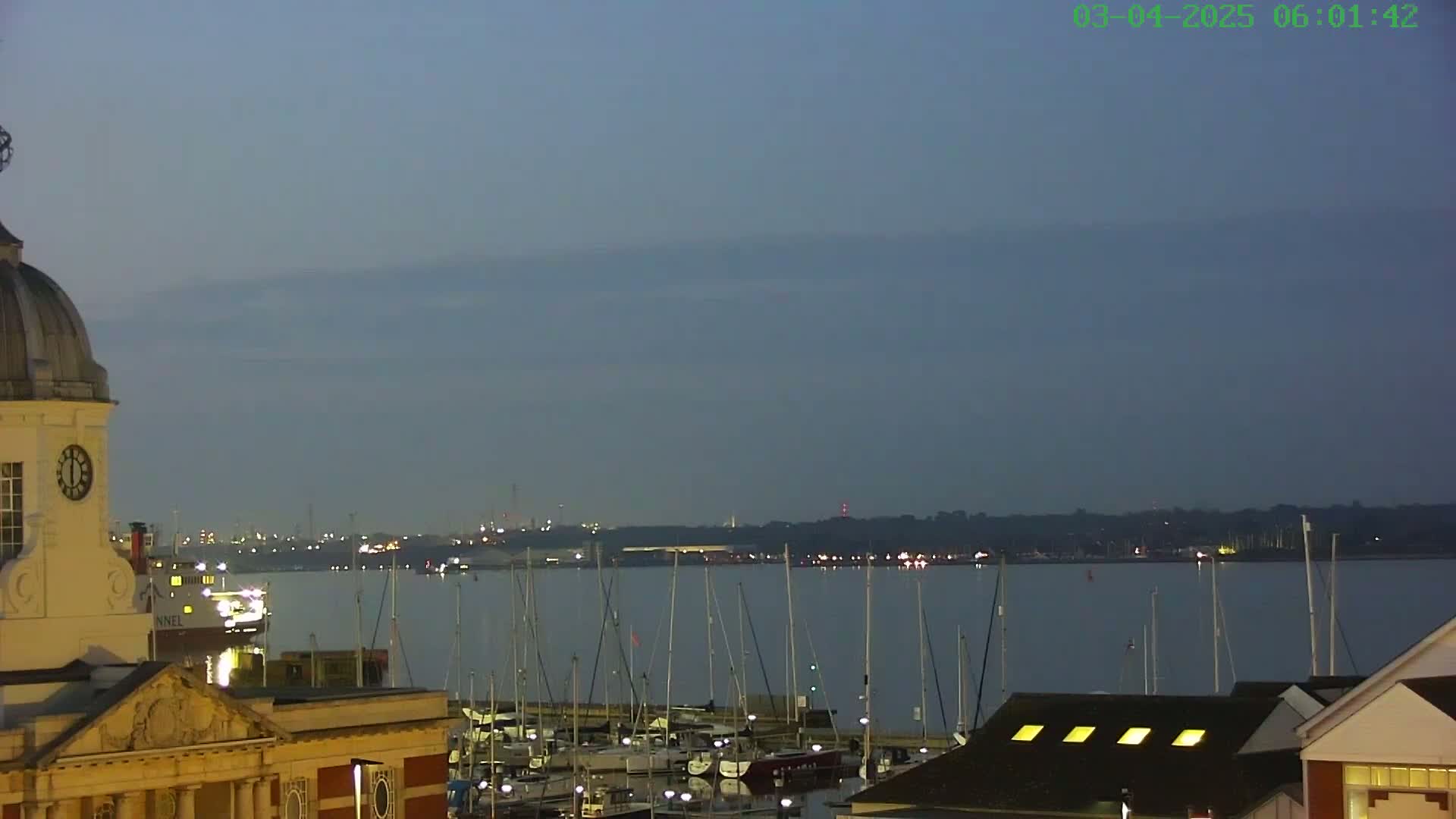 A harbor filled with docked sailboats is viewed from a building with a clock tower under a dusky sky.