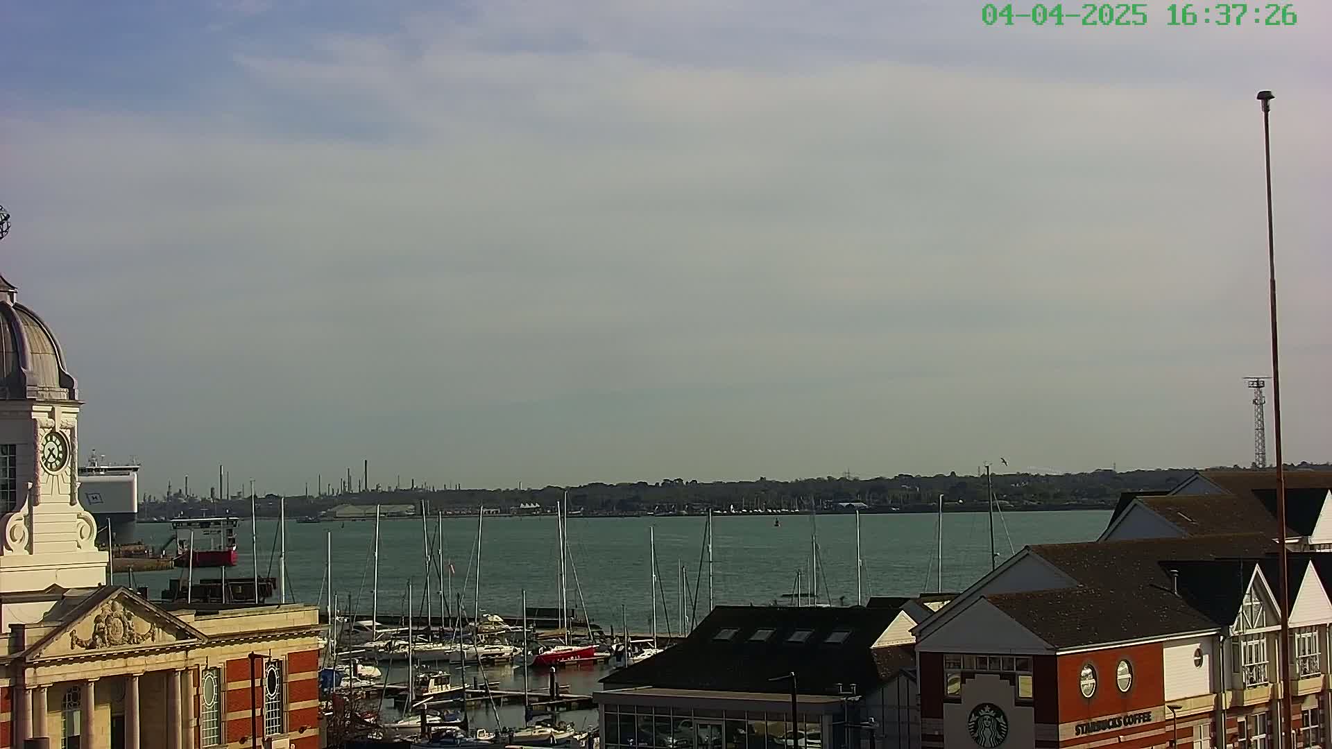 A harbor filled with sailboats is viewed from a building with a clock tower on a partly cloudy day.