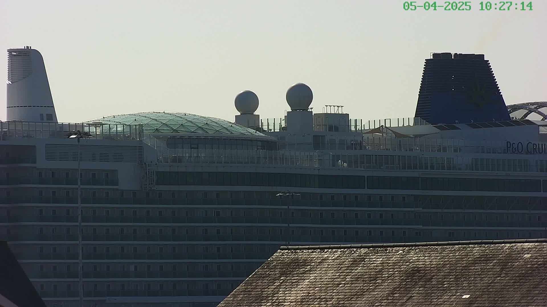 A large cruise ship is partially visible under a hazy sky, with a section of a dark roof in the bottom right corner.