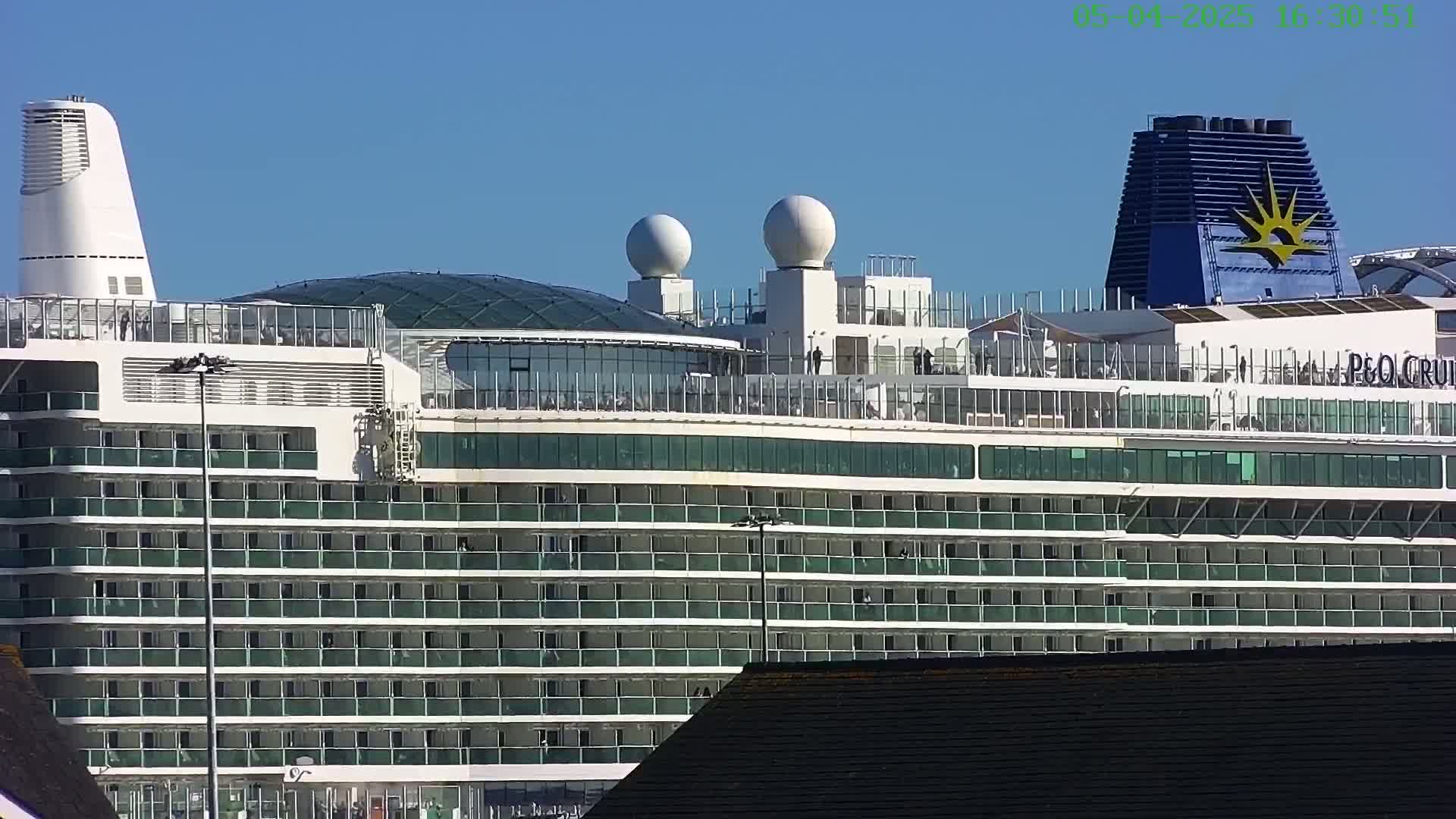 A large cruise ship with many balconies is docked under a clear blue sky.