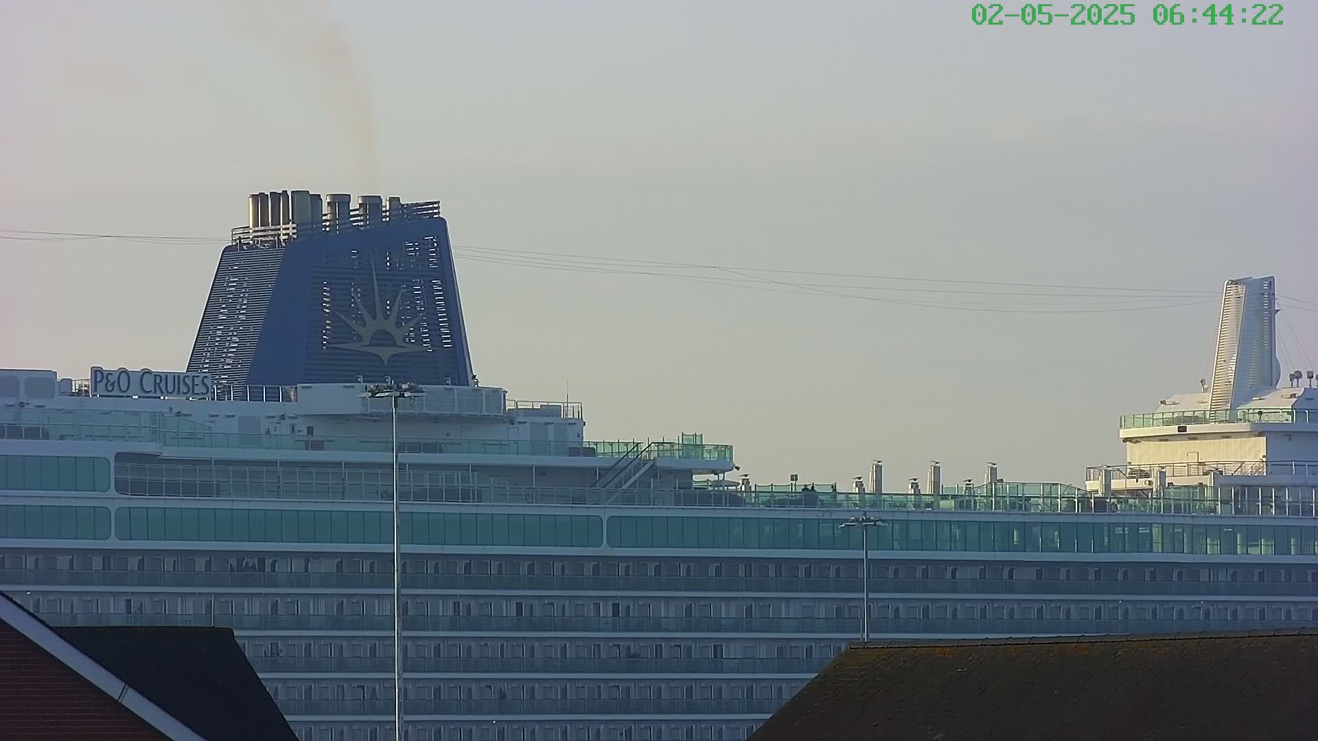A large cruise ship is docked, under a pale, overcast sky.
