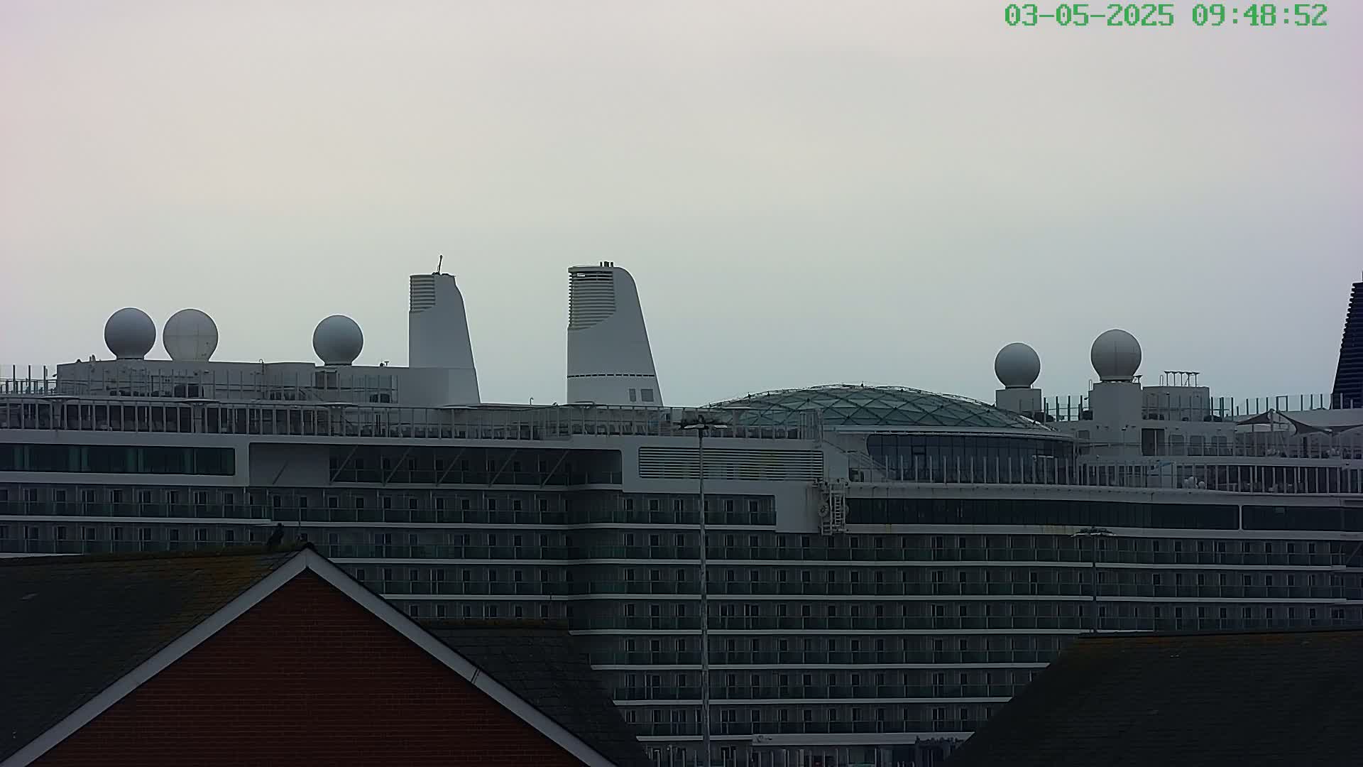 A large cruise ship with multiple radar domes and a glass-roofed structure is visible under an overcast sky.