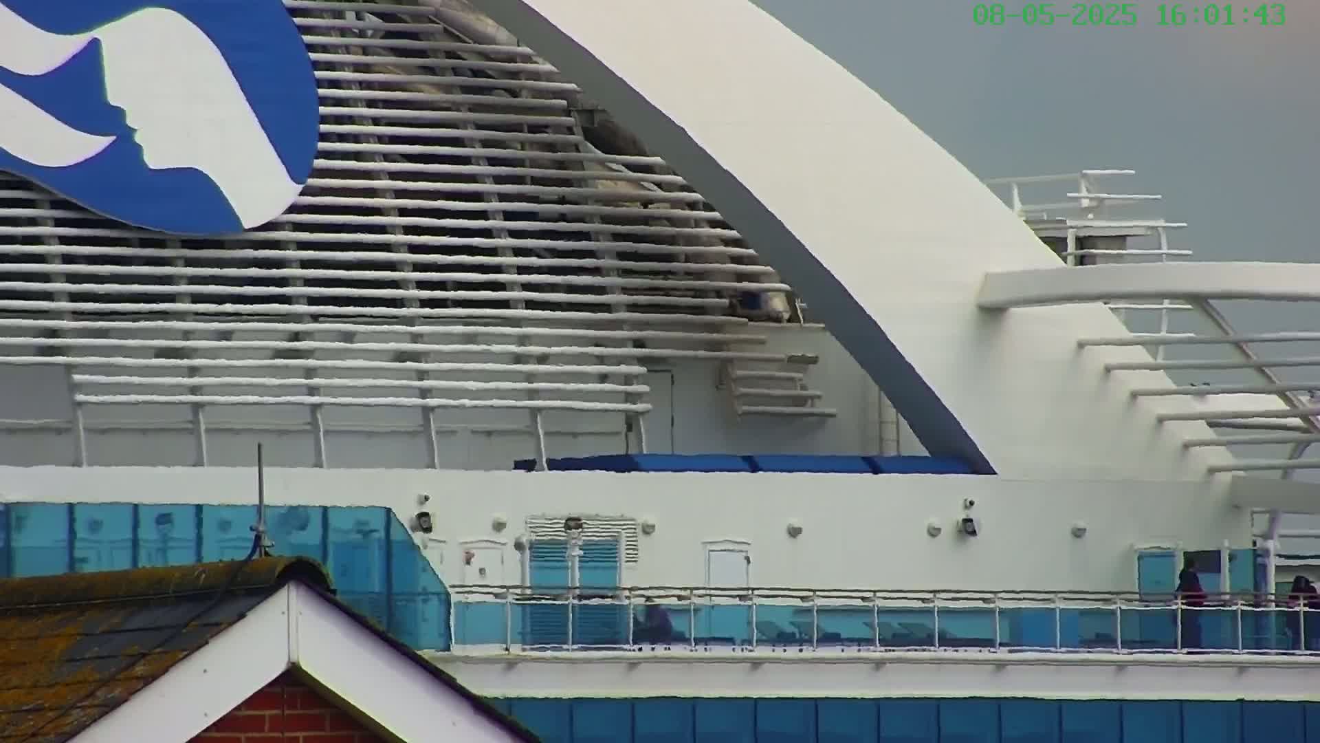 A portion of a large, white cruise ship with blue accents is visible, under an overcast sky.
