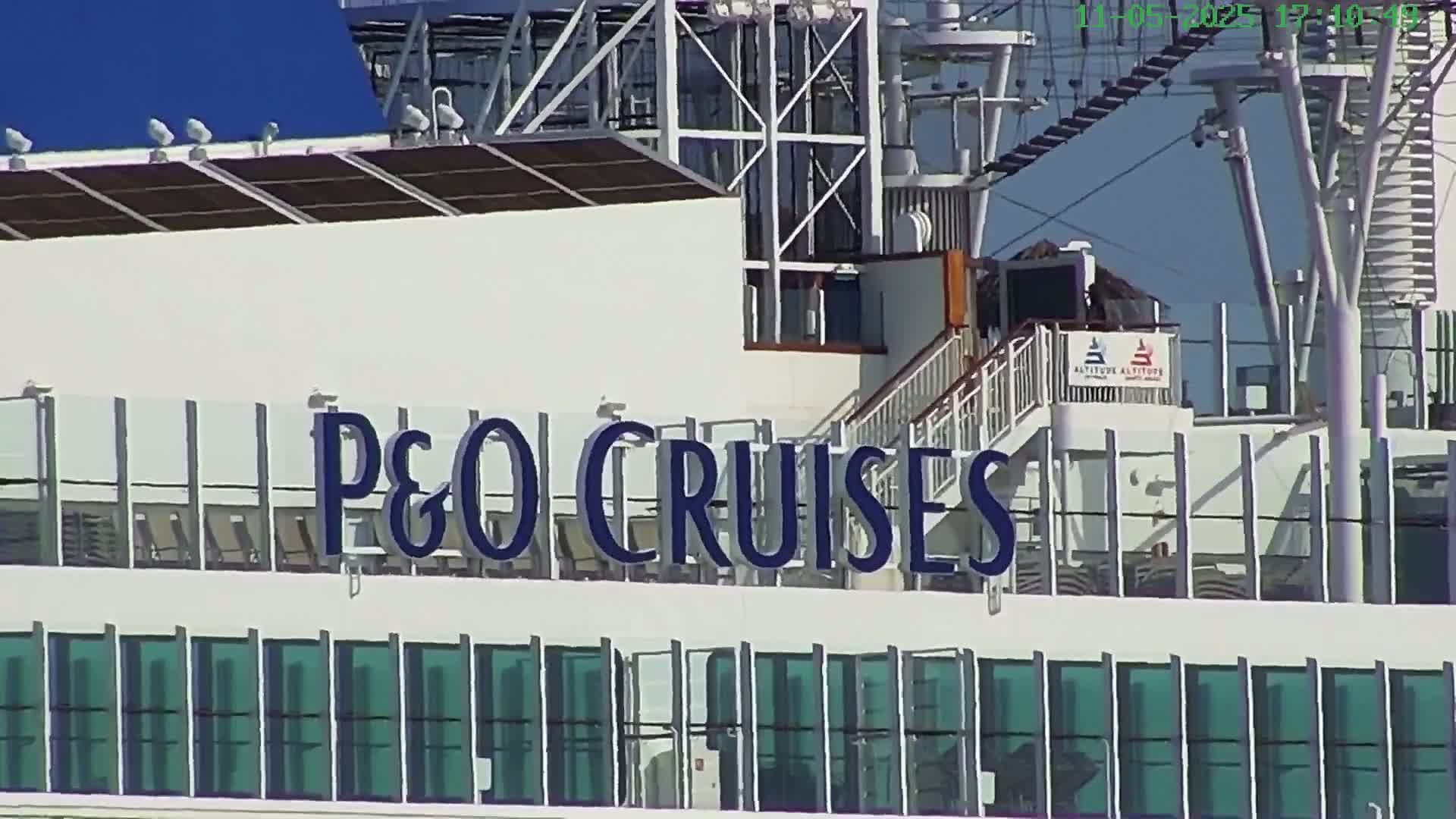 A portion of a P&O Cruises ship is visible under a clear blue sky, showing a deck with lounge chairs and numerous windows.