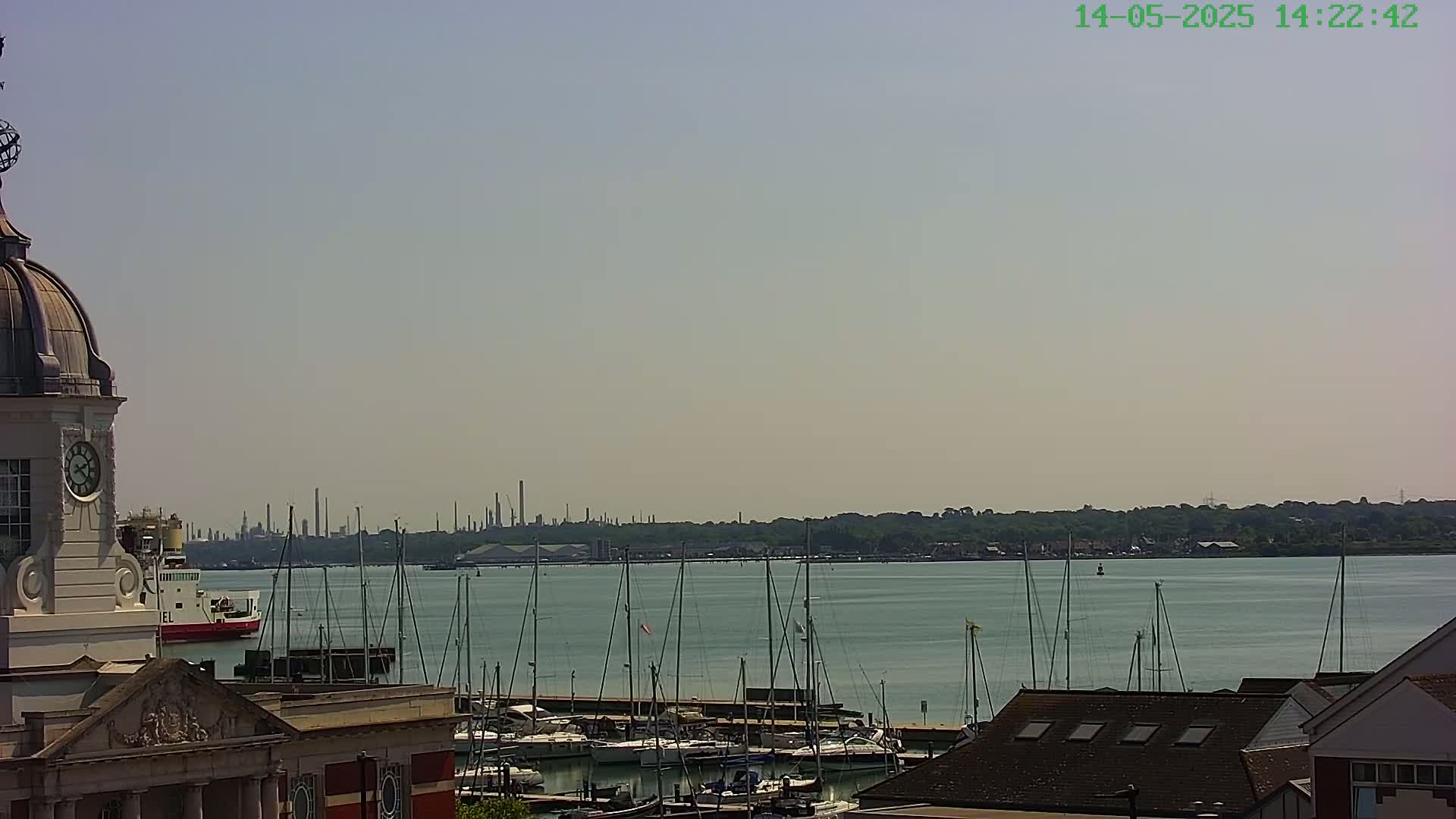 A view from a clock tower shows a harbor filled with sailboats, a distant industrial skyline, and a mostly clear sky.