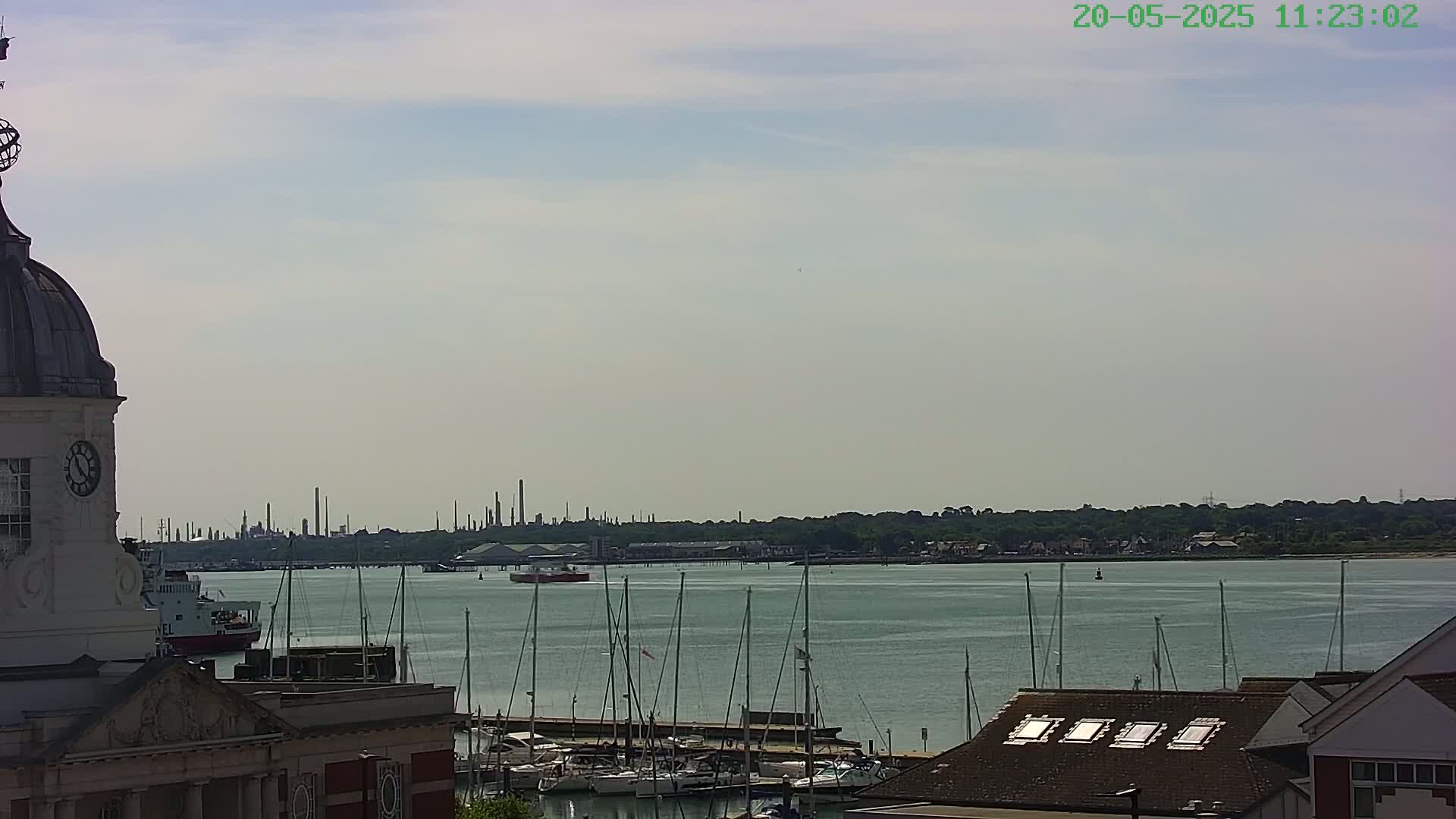 A partly cloudy day overlooks a harbor filled with sailboats and a distant industrial skyline.