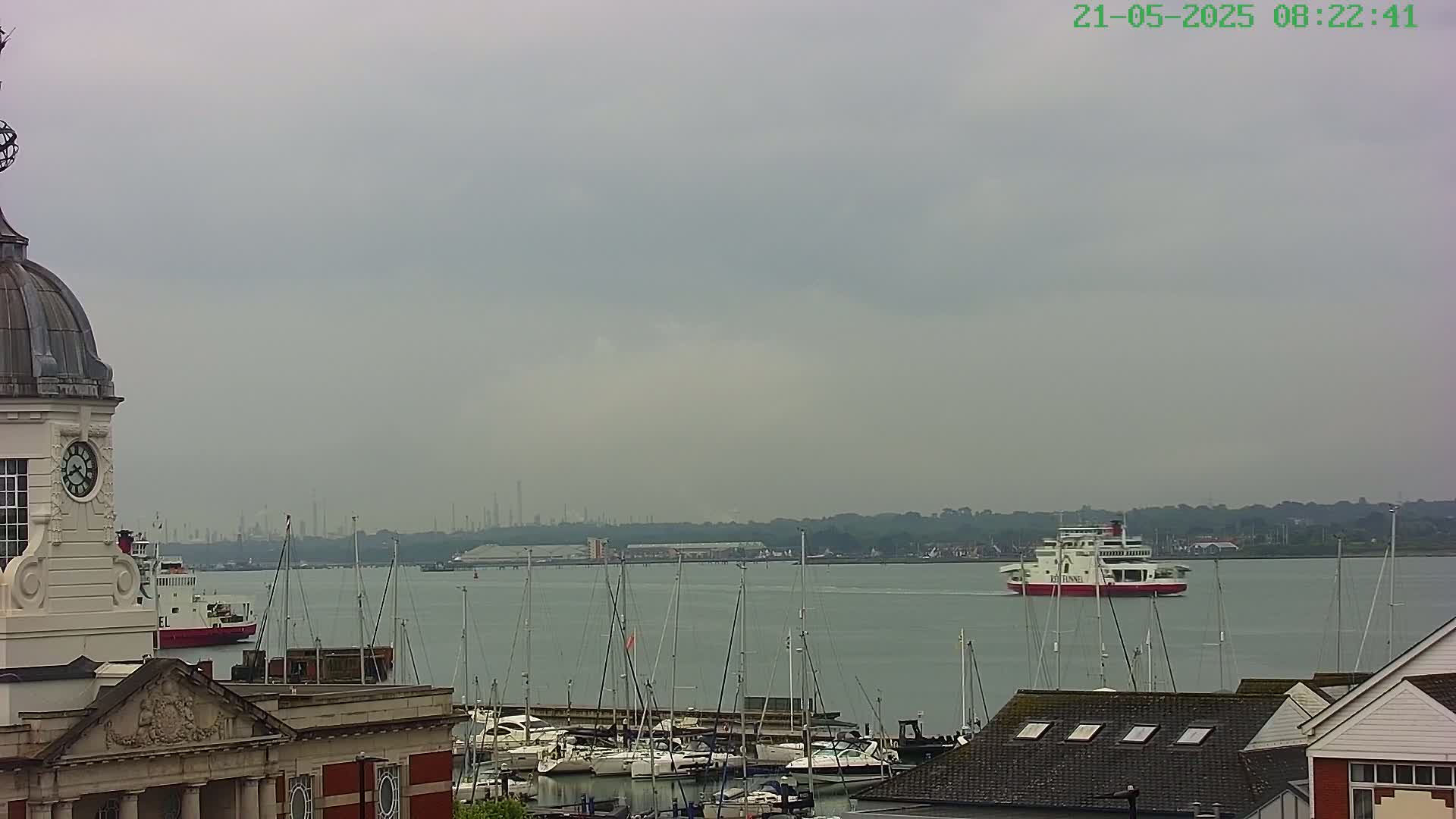 A gray, overcast day reveals a harbor filled with sailboats and a ferry in the distance, with a clock tower and buildings in the foreground.