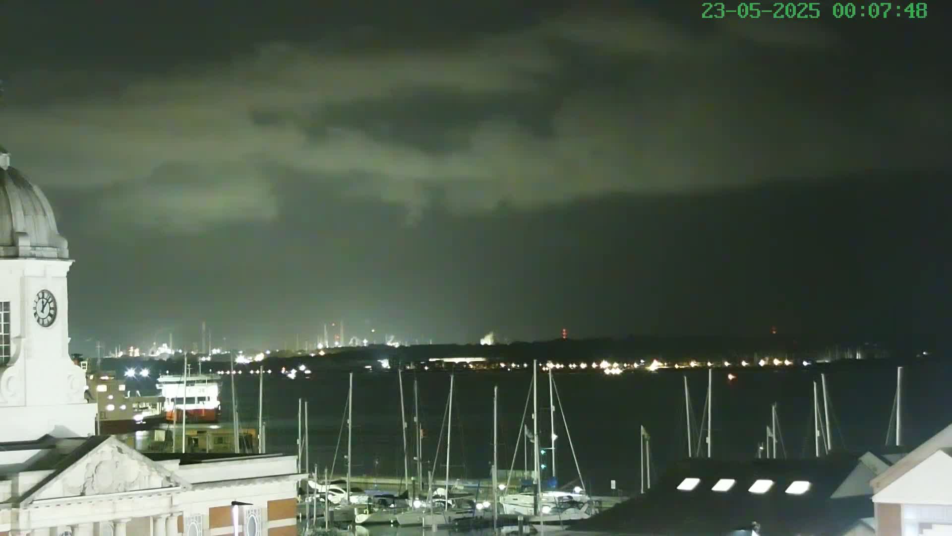 A nighttime view from a building with a clock tower overlooking a harbor filled with sailboats under a cloudy sky.