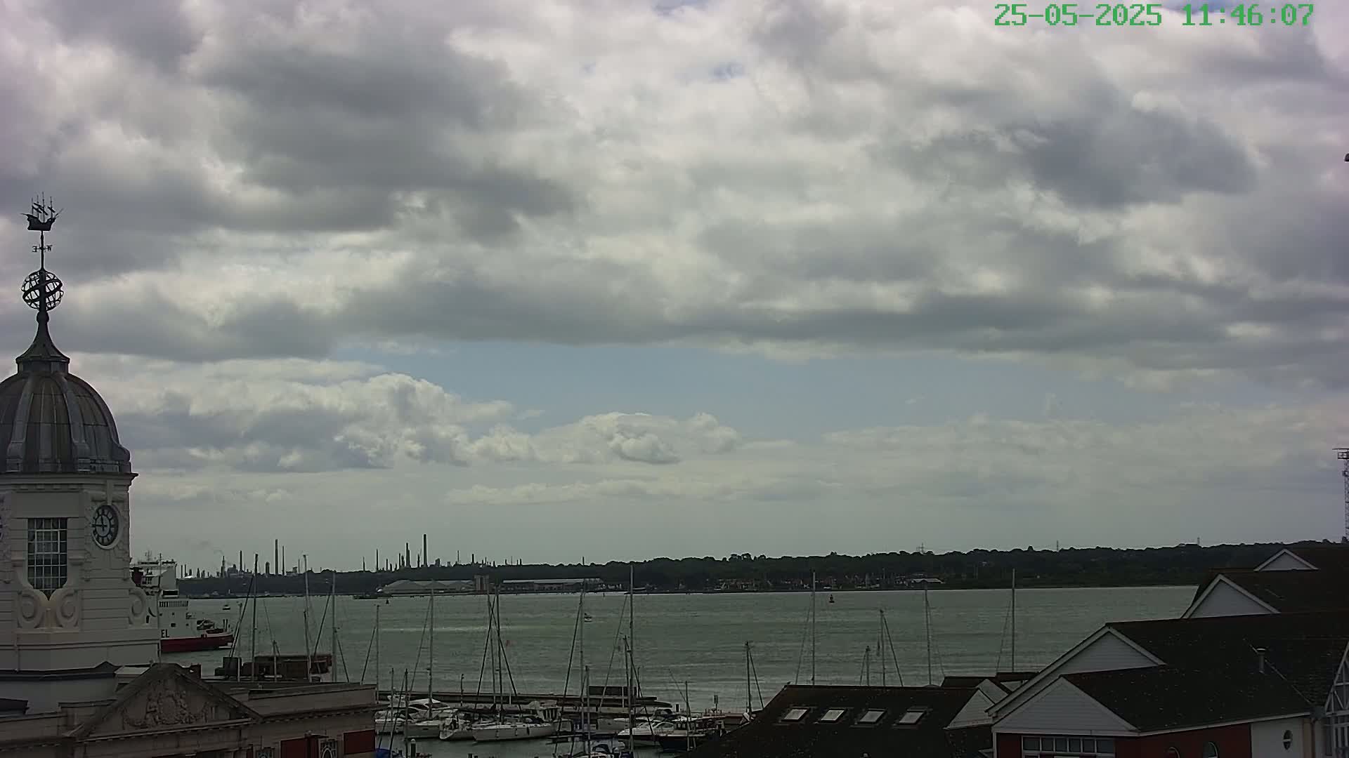 A harbor scene under a cloudy sky shows numerous sailboats docked and a clock tower in the foreground with a distant industrial skyline.