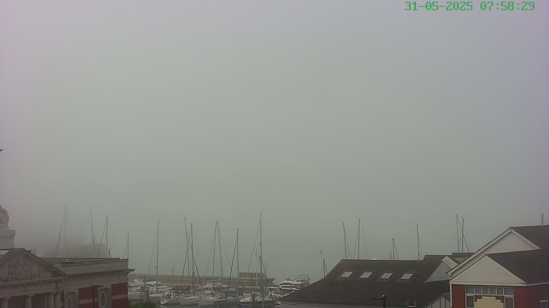 A foggy harbor scene shows numerous sailboats moored at a dock, partially obscured by the thick fog, with buildings in the foreground.