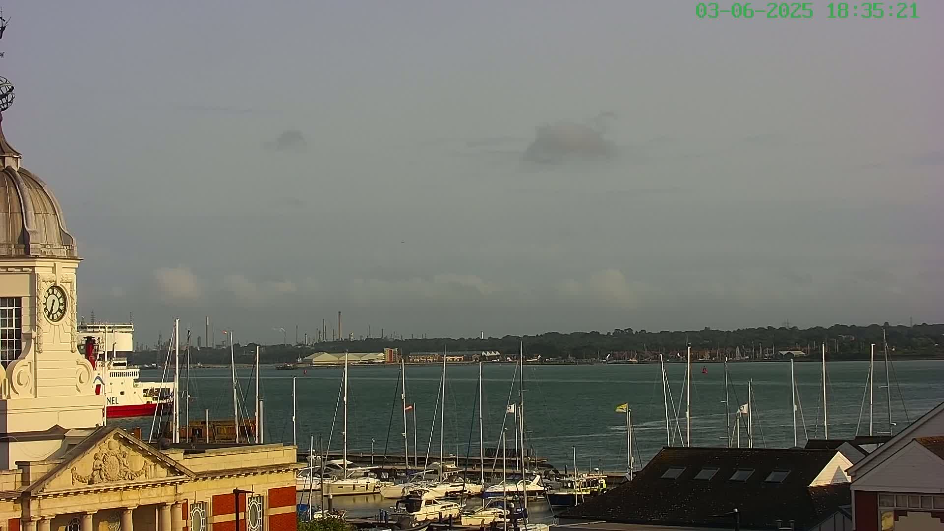 A clock tower overlooks a harbor filled with sailboats under a mostly cloudy sky.