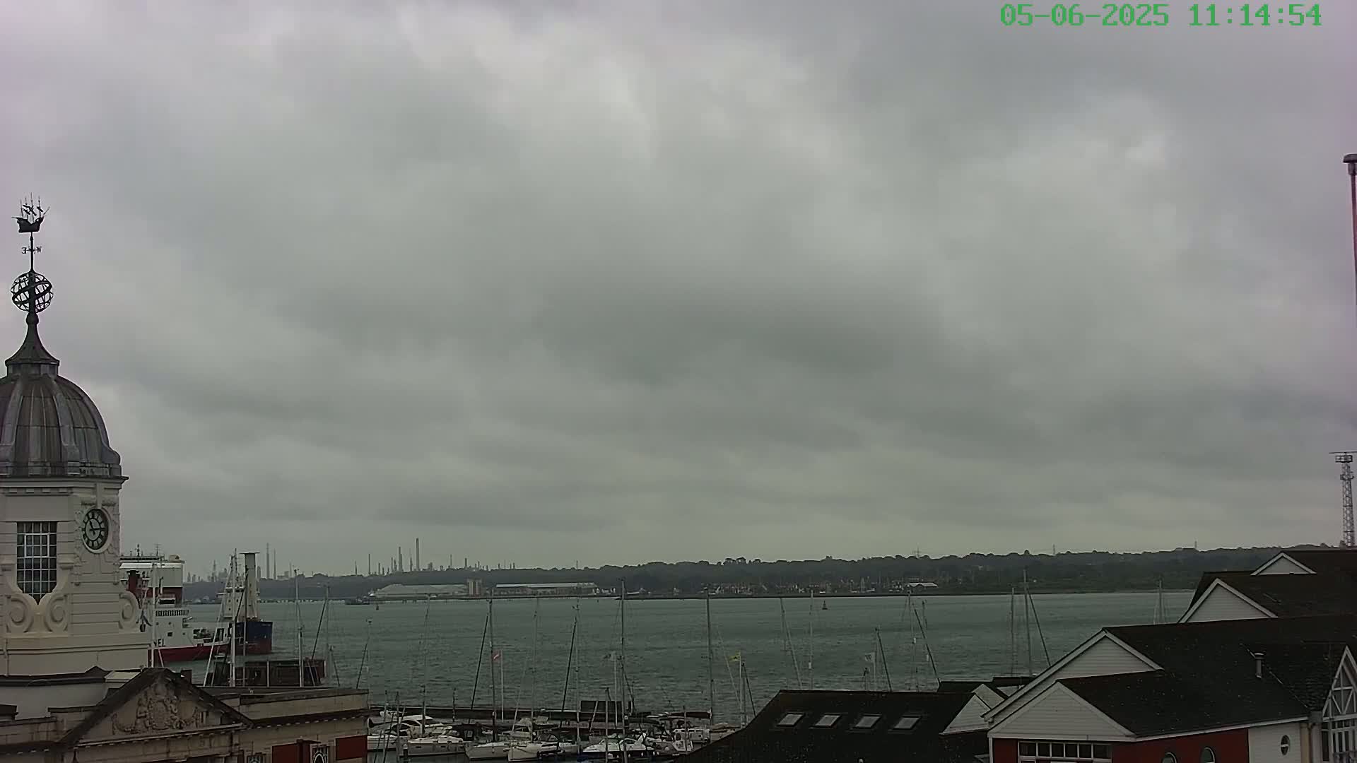 A view of a harbor with numerous boats and a distant industrial shoreline under an overcast sky.