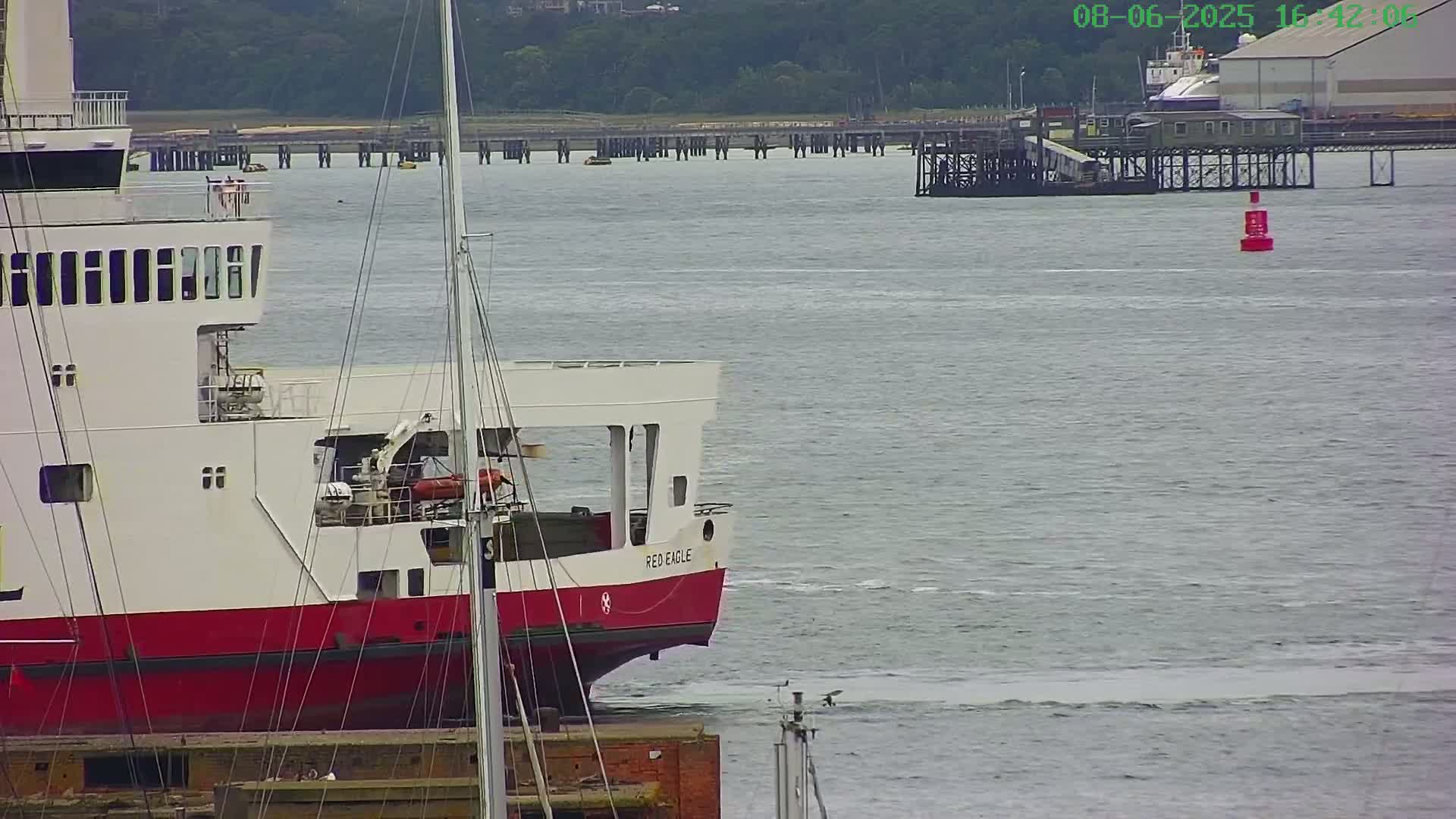 A red and white ferry named "Red Eagle" is docked near a pier on a calm, gray day.