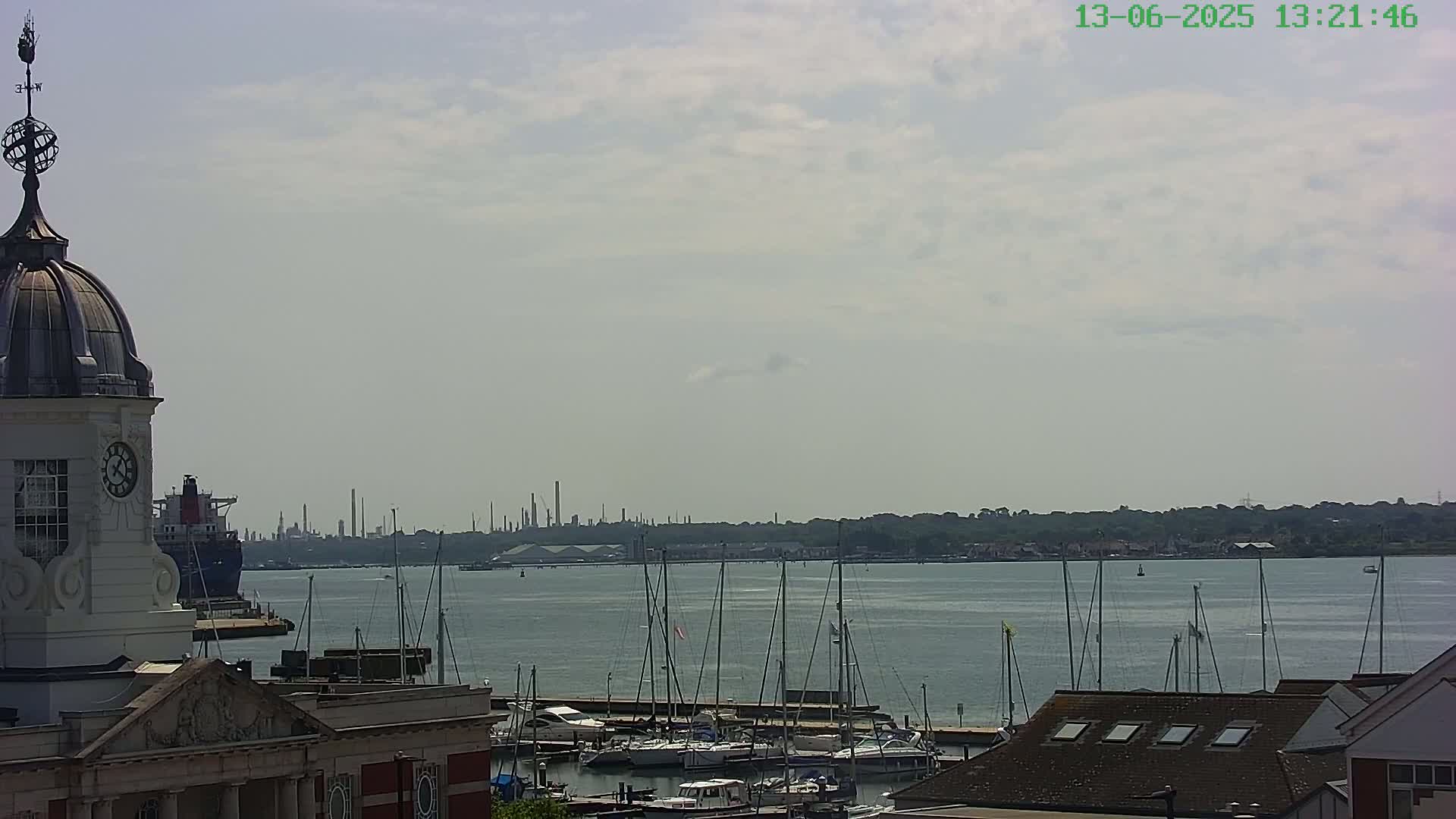 A view from atop a building shows a harbor filled with sailboats, a large ship in the distance, and an industrial area on the horizon under a partly cloudy sky.