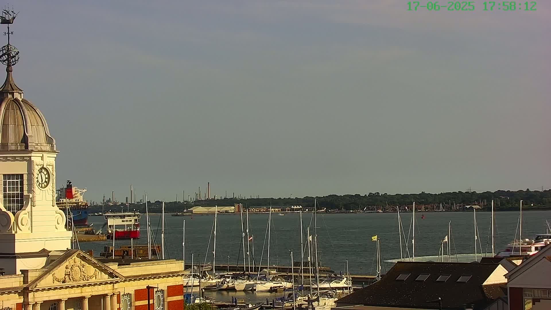 A clock tower overlooks a harbor filled with sailboats under a hazy sky.