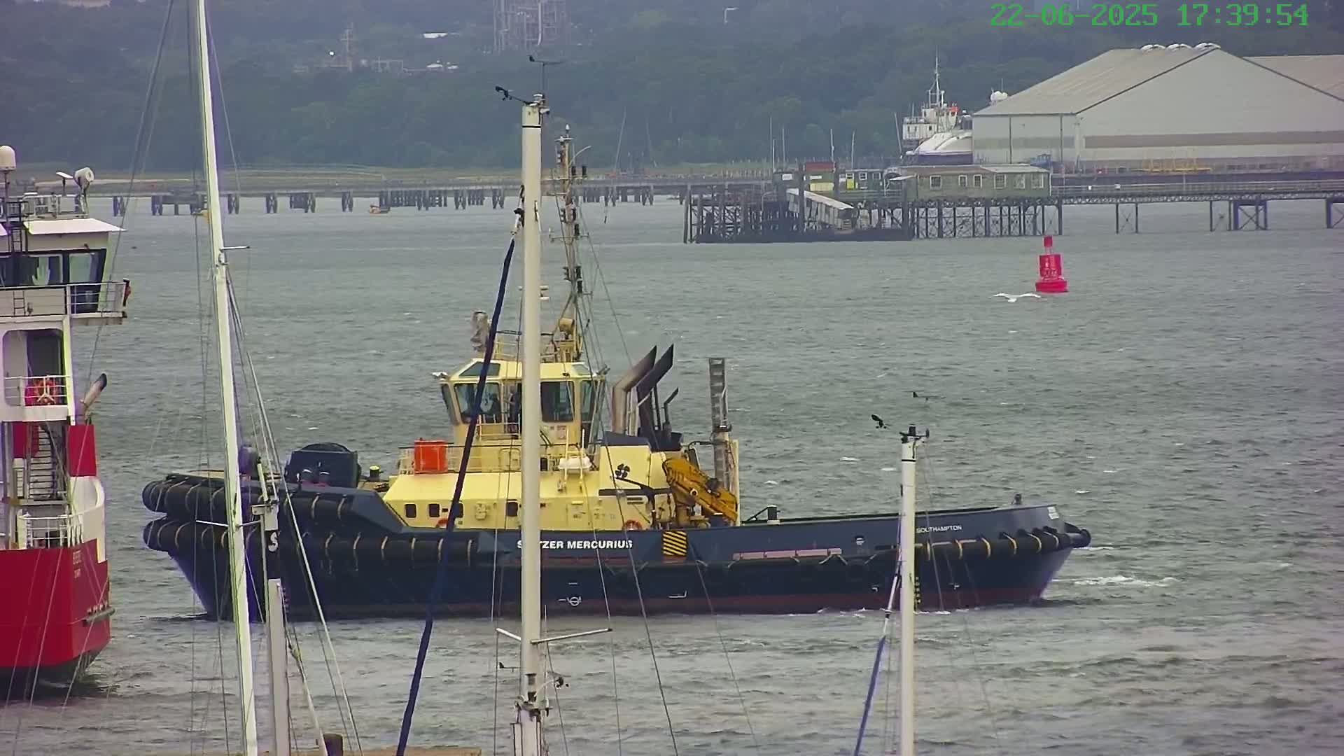 A tugboat is on the water near a pier and other boats on a slightly overcast day.