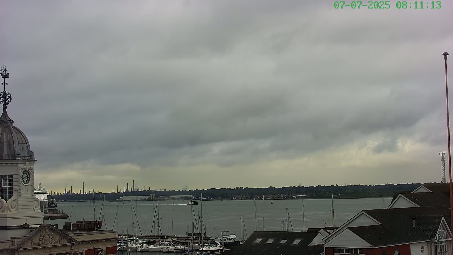 A harbor scene under an overcast sky shows a clock tower, numerous boats, and a distant industrial area.