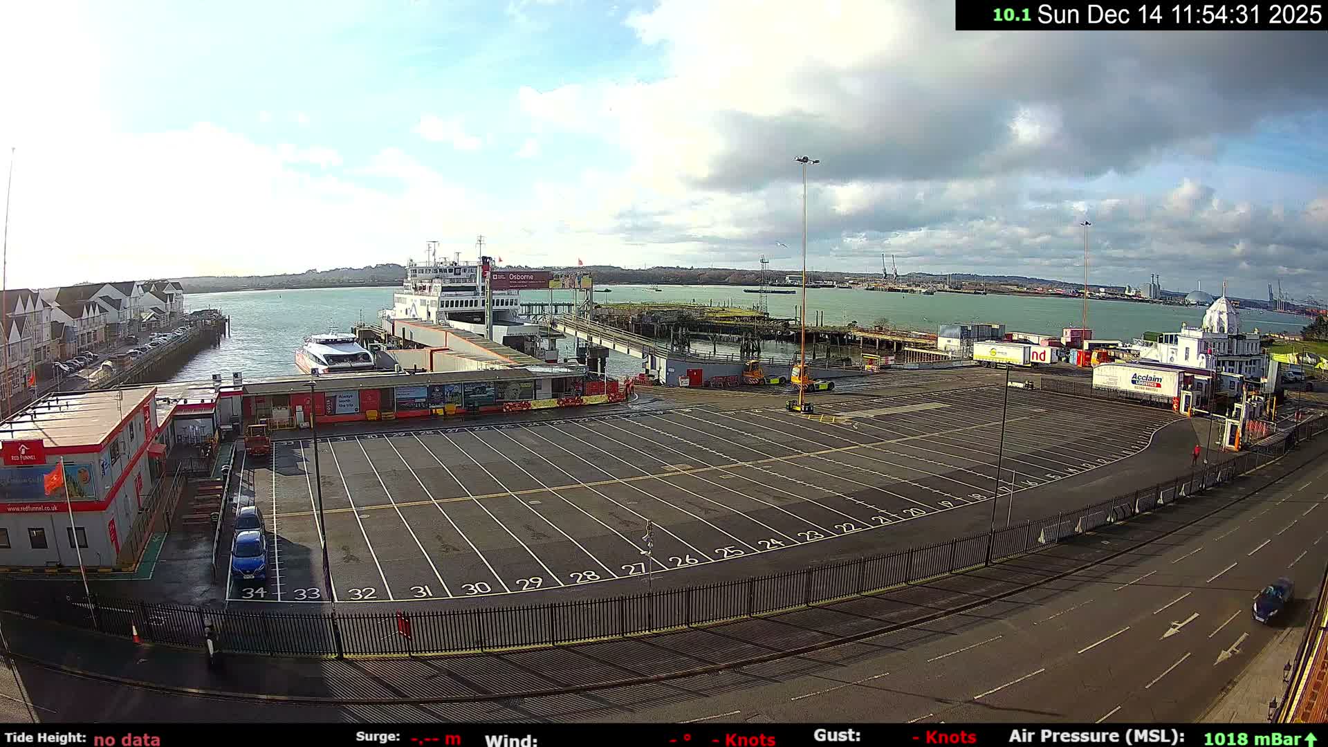 A dramatic sunrise casts a golden glow across a bustling harbor, illuminating numerous sailboats, a prominent clock tower, and distant industrial silhouettes under a sky filled with dark, heavy clouds interspersed with bright yellow hues.