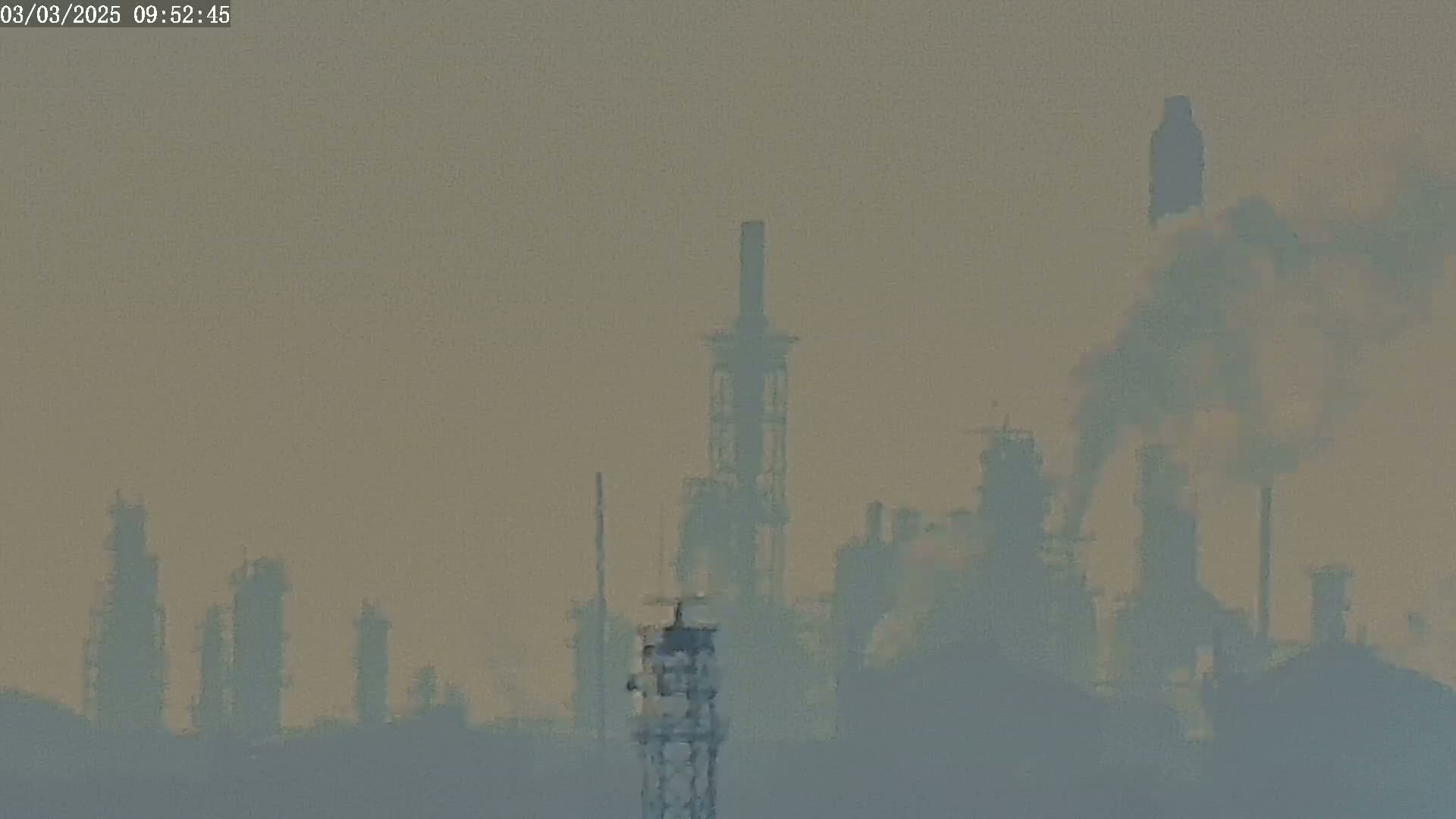 A hazy view of an industrial plant with several tall structures emitting smoke into a muted sky.