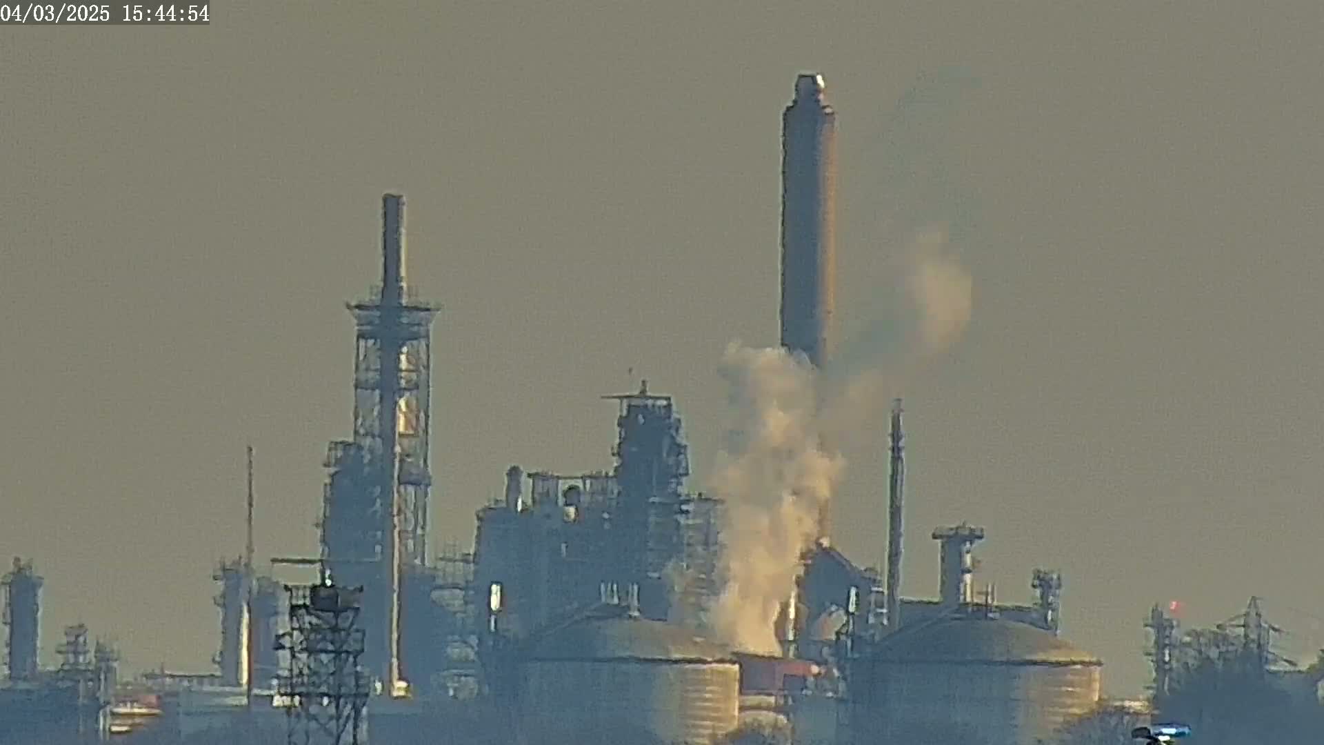 A hazy view of an industrial complex with several tall smokestacks emitting smoke into the air.