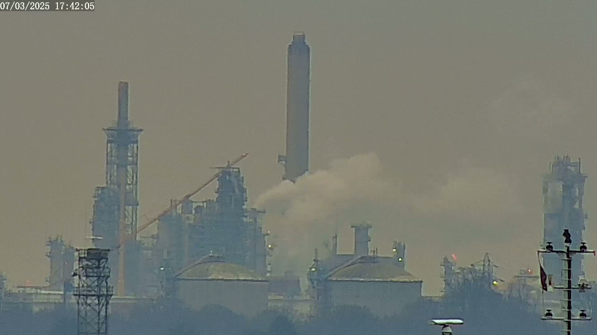 A hazy view of an industrial complex with tall smokestacks emitting smoke and steam into the air.