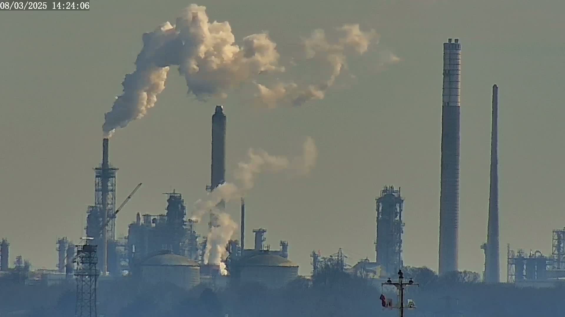 A hazy industrial complex with several tall smokestacks emitting plumes of smoke is visible in the distance.