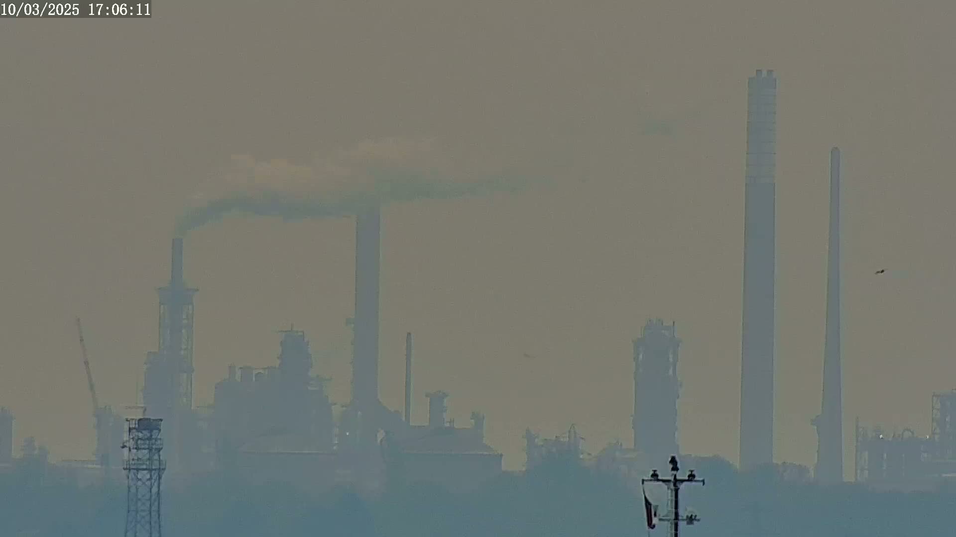 A hazy, industrial landscape is visible, featuring several tall smokestacks emitting plumes of smoke.