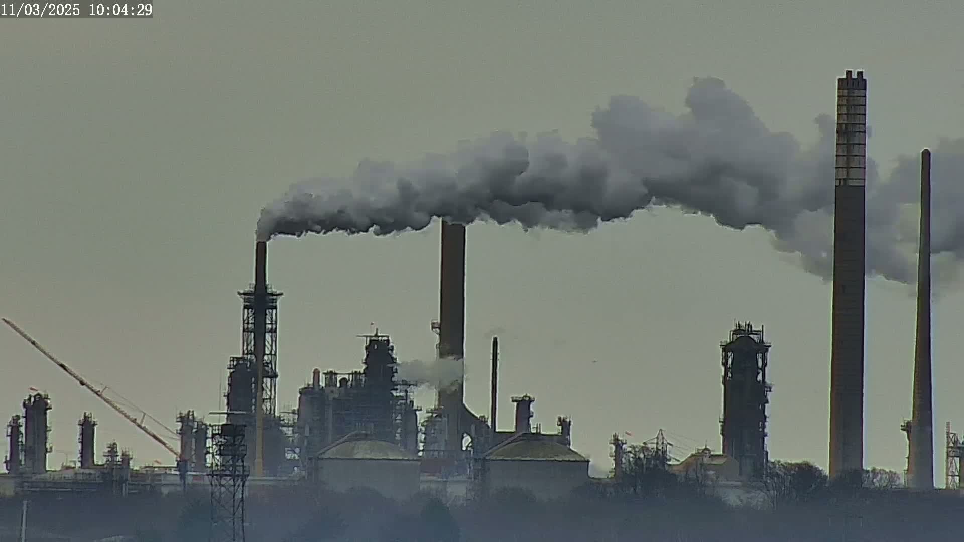 A large industrial complex with numerous smokestacks emitting plumes of dark smoke into an overcast sky.